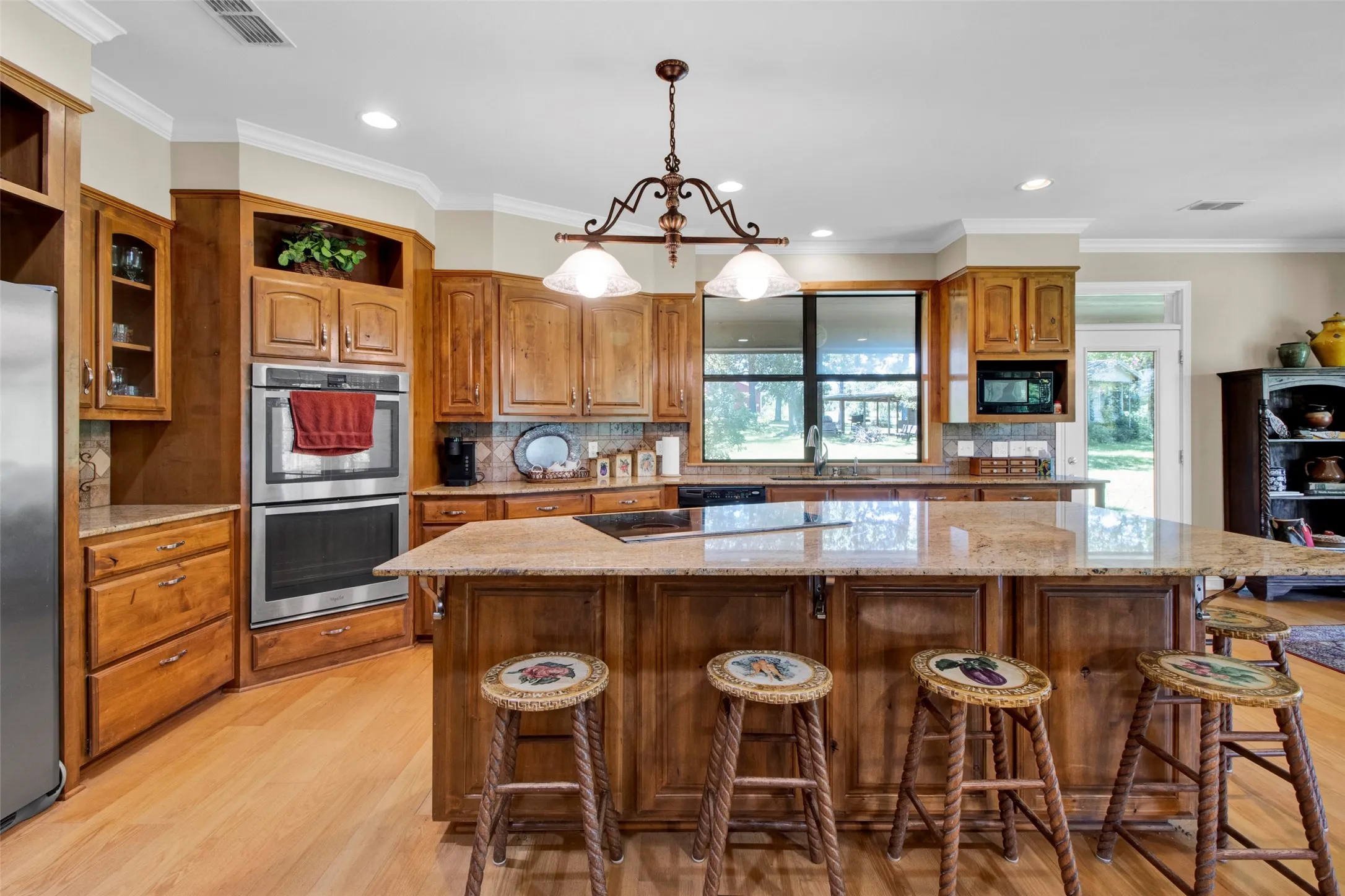 Spacious kitchen featuring warm wood cabinetry, light granite countertops, stainless steel double ovens, a center island, and wood-finish flooring