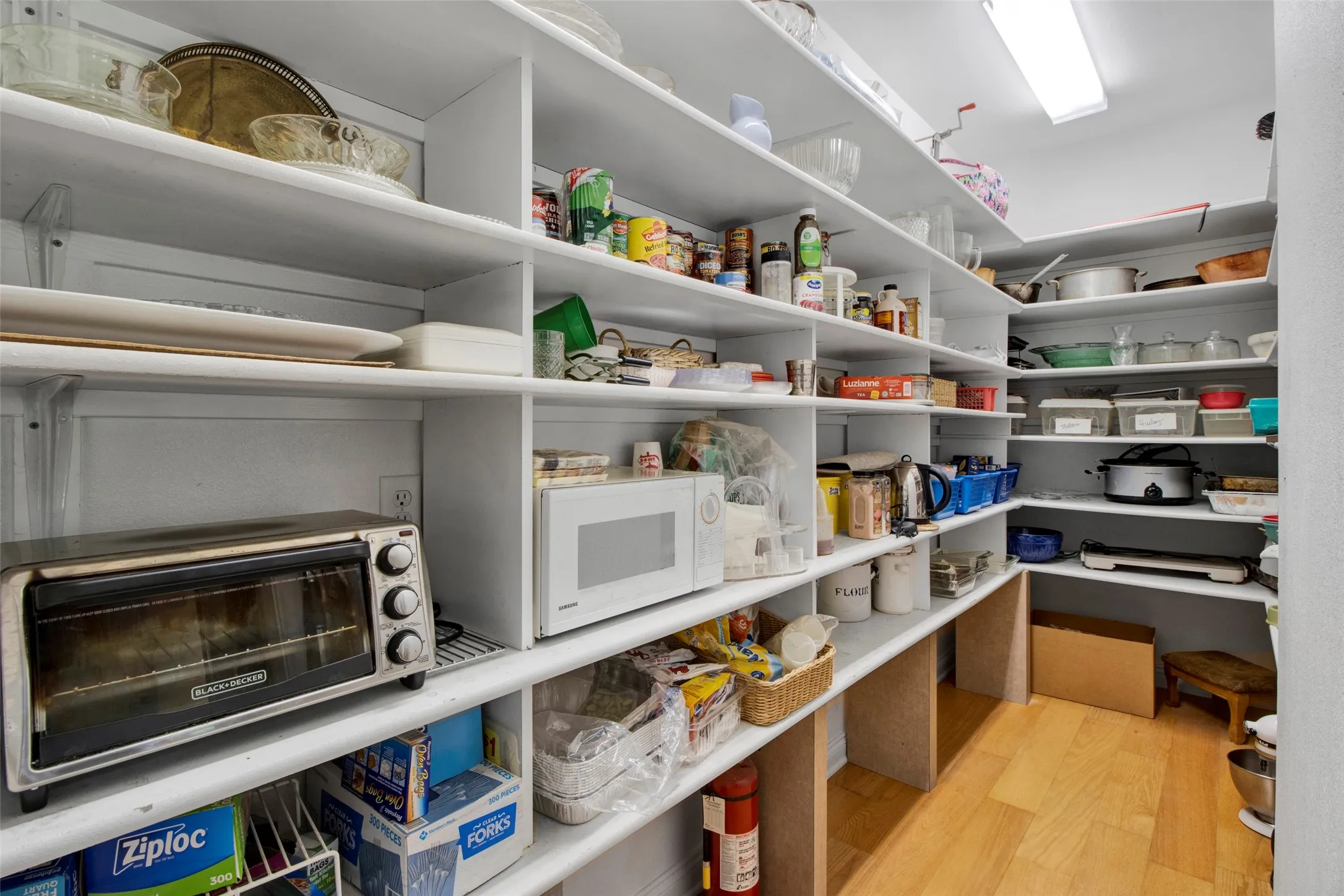 The literal Walk-in pantry featuring extensive white shelving, wood-finish flooring, and integrated countertop space