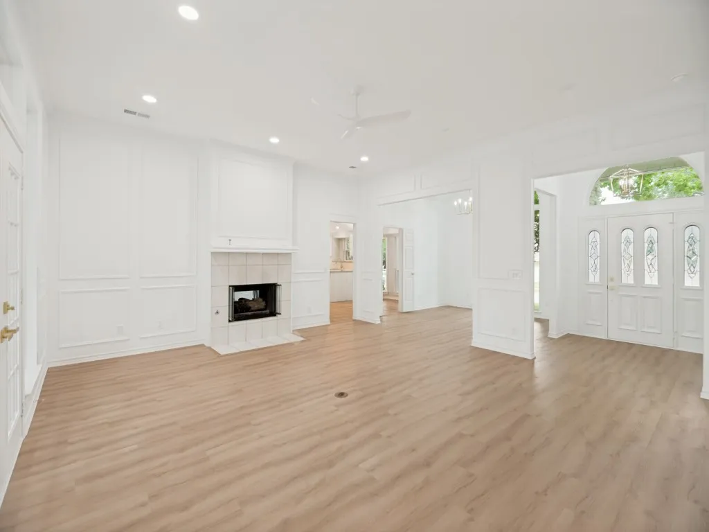 Expansive interior space featuring light wood-finish flooring, a tile-surround fireplace with hearth, recessed lighting, and decorative wall molding