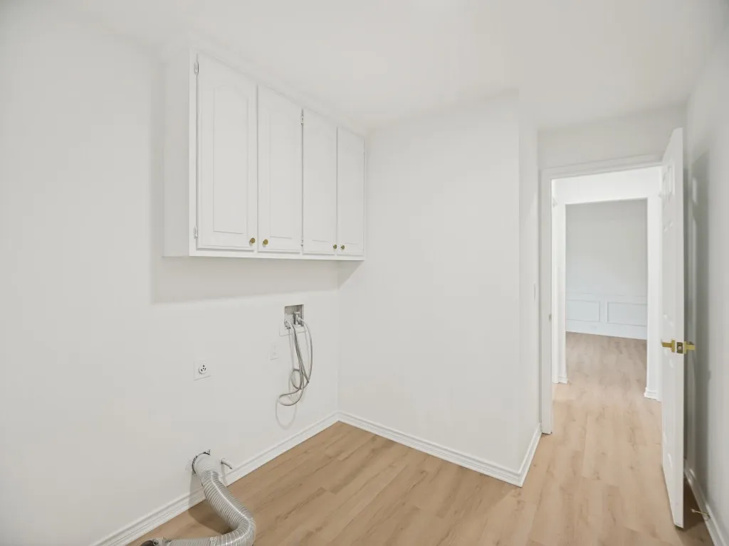 Laundry area featuring light wood-finish flooring, white cabinetry with brass-finish hardware, and crisp white walls