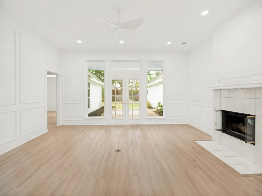 Light-filled living area featuring wood-finish flooring, a tiled fireplace with glass enclosure, and French doors opening to the exterior