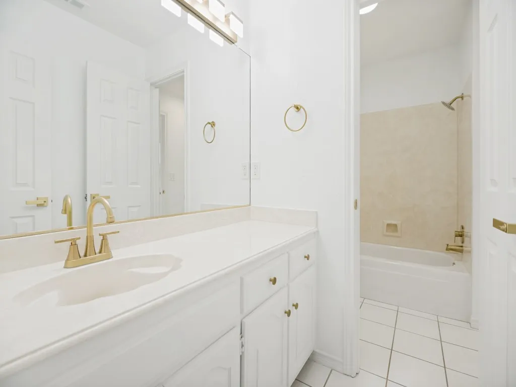 Bathroom featuring a white vanity with gold-finish hardware, integrated sink, and full-width mirror