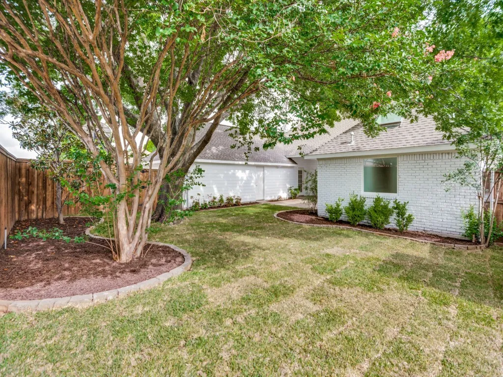 Spacious backyard featuring a substantial tree with textured bark, a manicured lawn, and a white brick exterior
