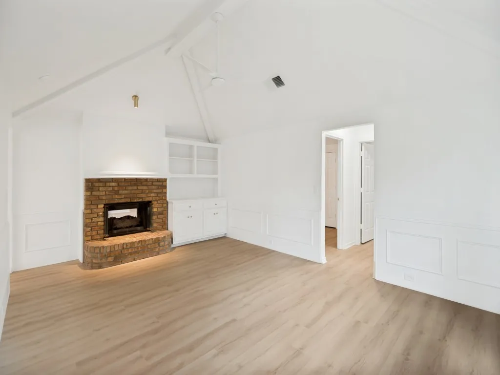 Spacious living area featuring a brick fireplace, built-in cabinetry, wood-finish flooring, wainscoting, and a vaulted ceiling