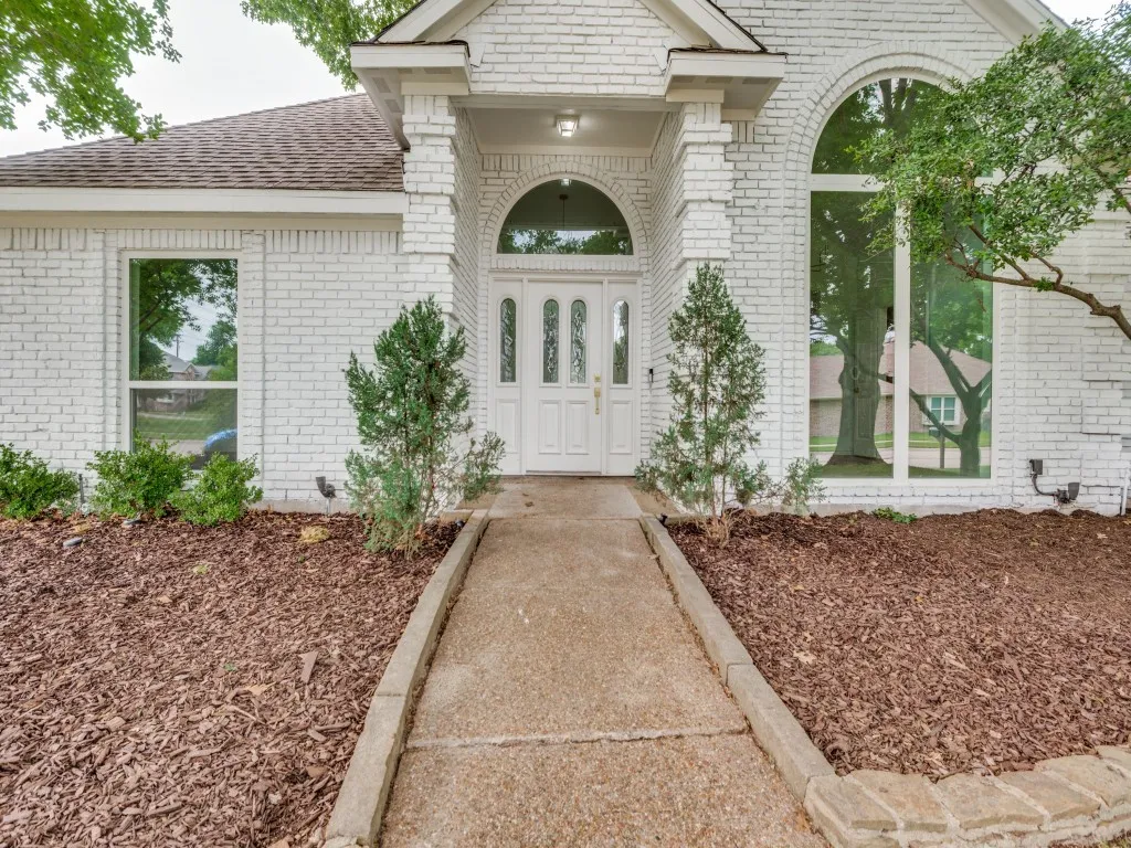 White brick exterior with a prominent arched entry, featuring a double door with decorative glass inserts