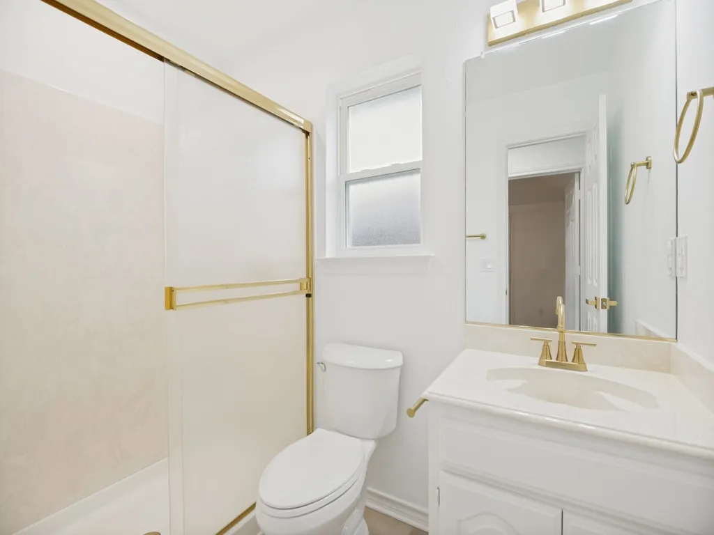 Full bathroom featuring a shower with gold-toned sliding doors, a vanity with a drop-in sink and gold-toned faucet, a large wall-mounted mirror, and a window with privacy glass