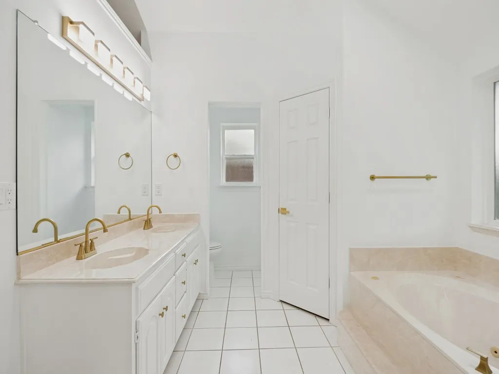Bathroom featuring a double vanity with built-in sinks, light-toned countertop, and gold-finish fixtures