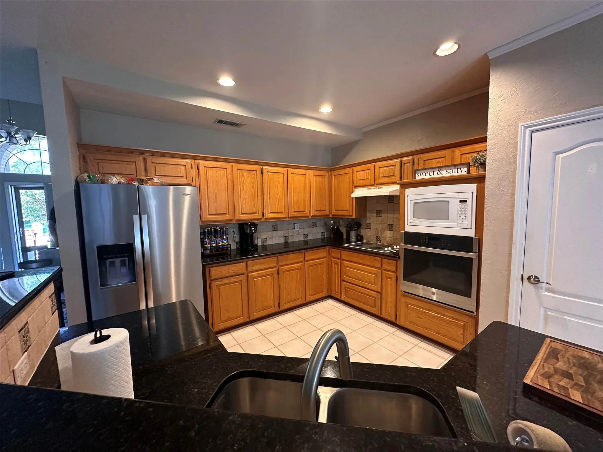 Kitchen featuring wood cabinetry, dark countertops, tiled backsplash, and stainless steel appliances including a double-door refrigerator and built-in oven with microwave