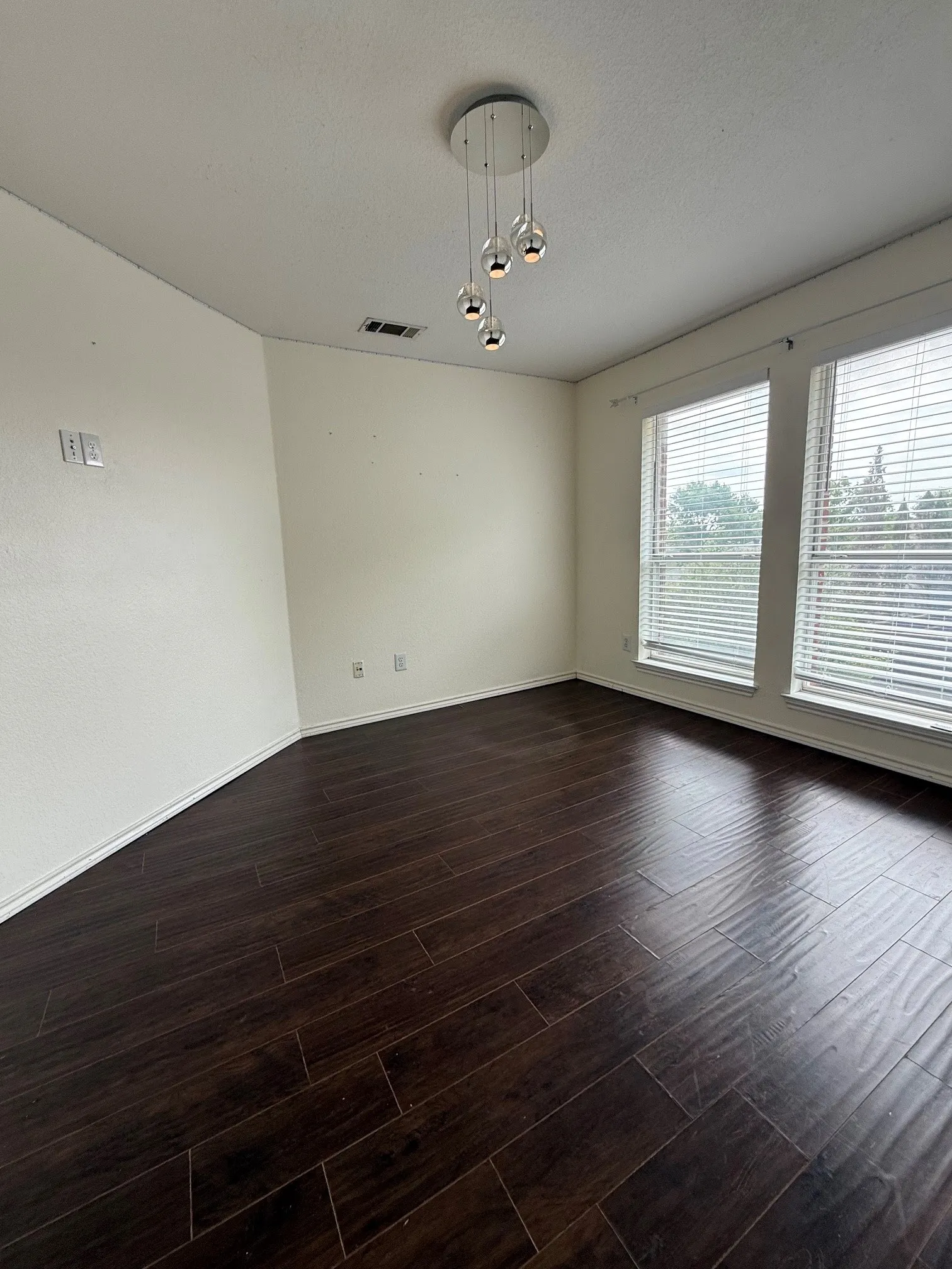 Spacious bedroom featuring dark wood-finish flooring, white walls, and a contemporary multi-bulb pendant light fixture