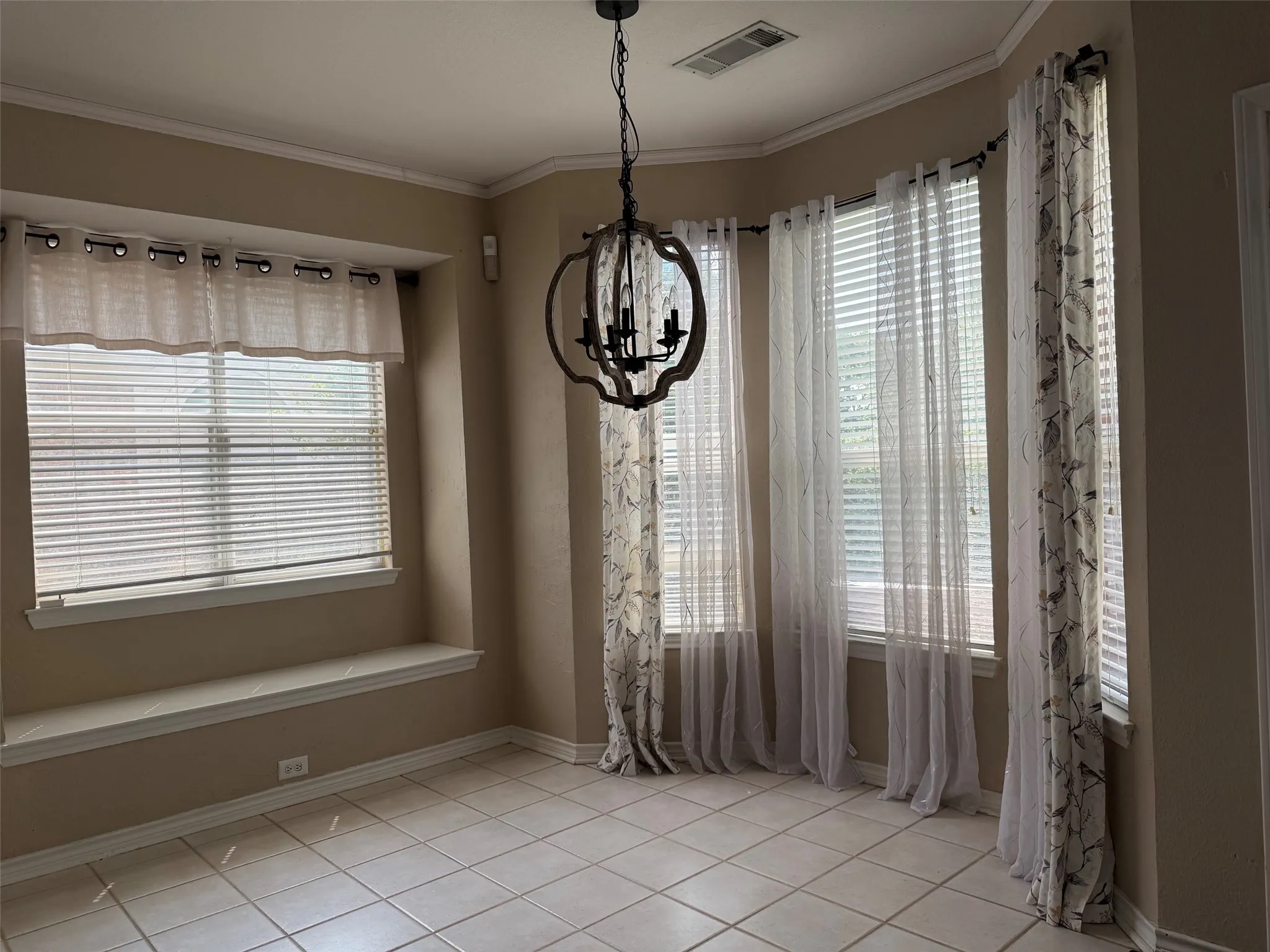 Dining area with a multi-paned bay window, a built-in window seat, a decorative chandelier, tile flooring, and crown molding
