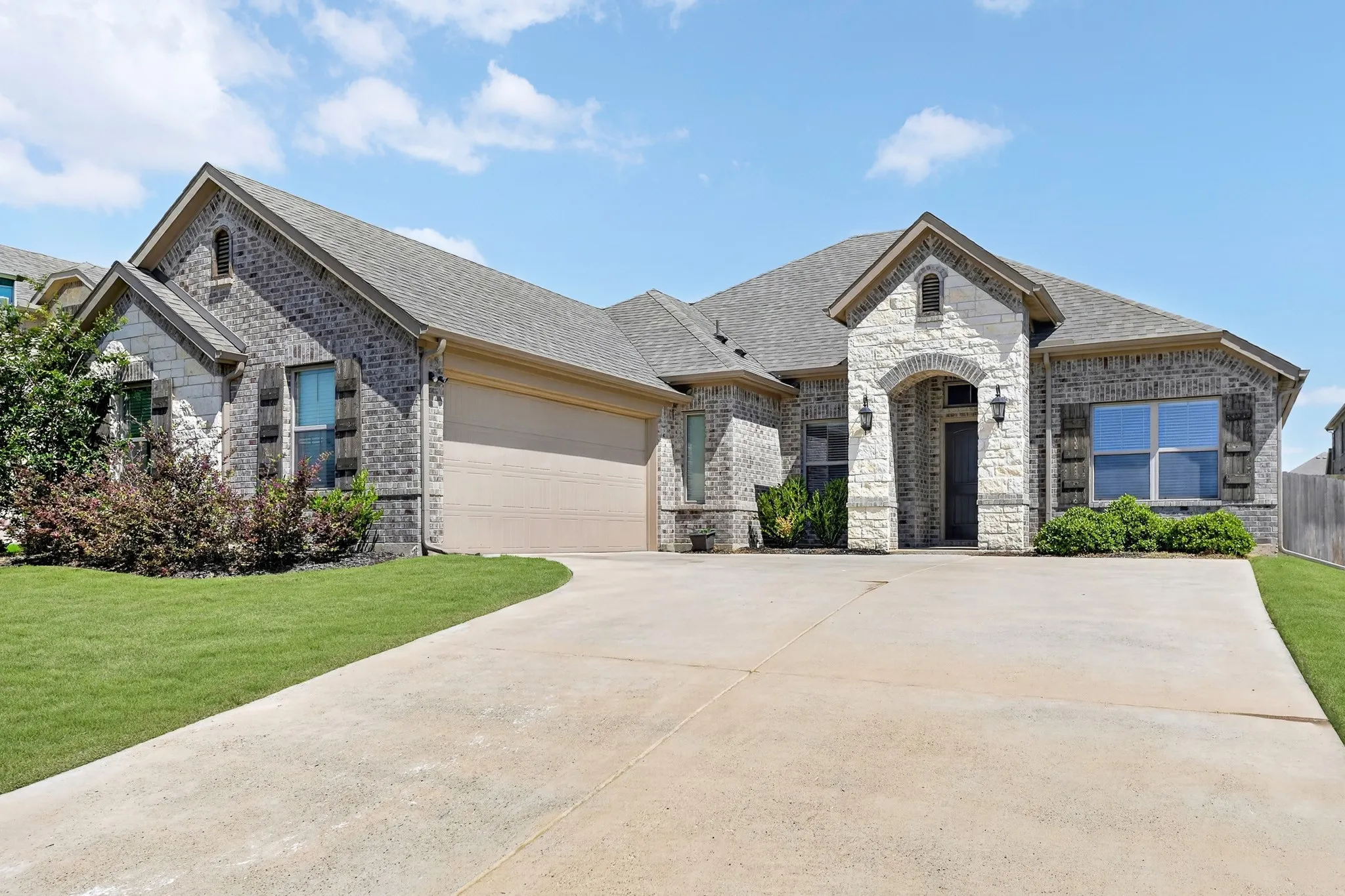 Brick and stone facade featuring an arched entry, a two-car garage, and a concrete driveway