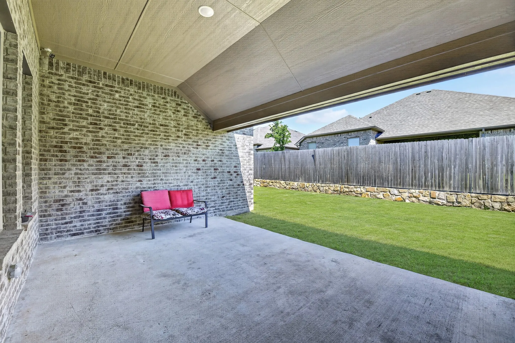 Covered patio featuring a concrete slab and exposed brick wall