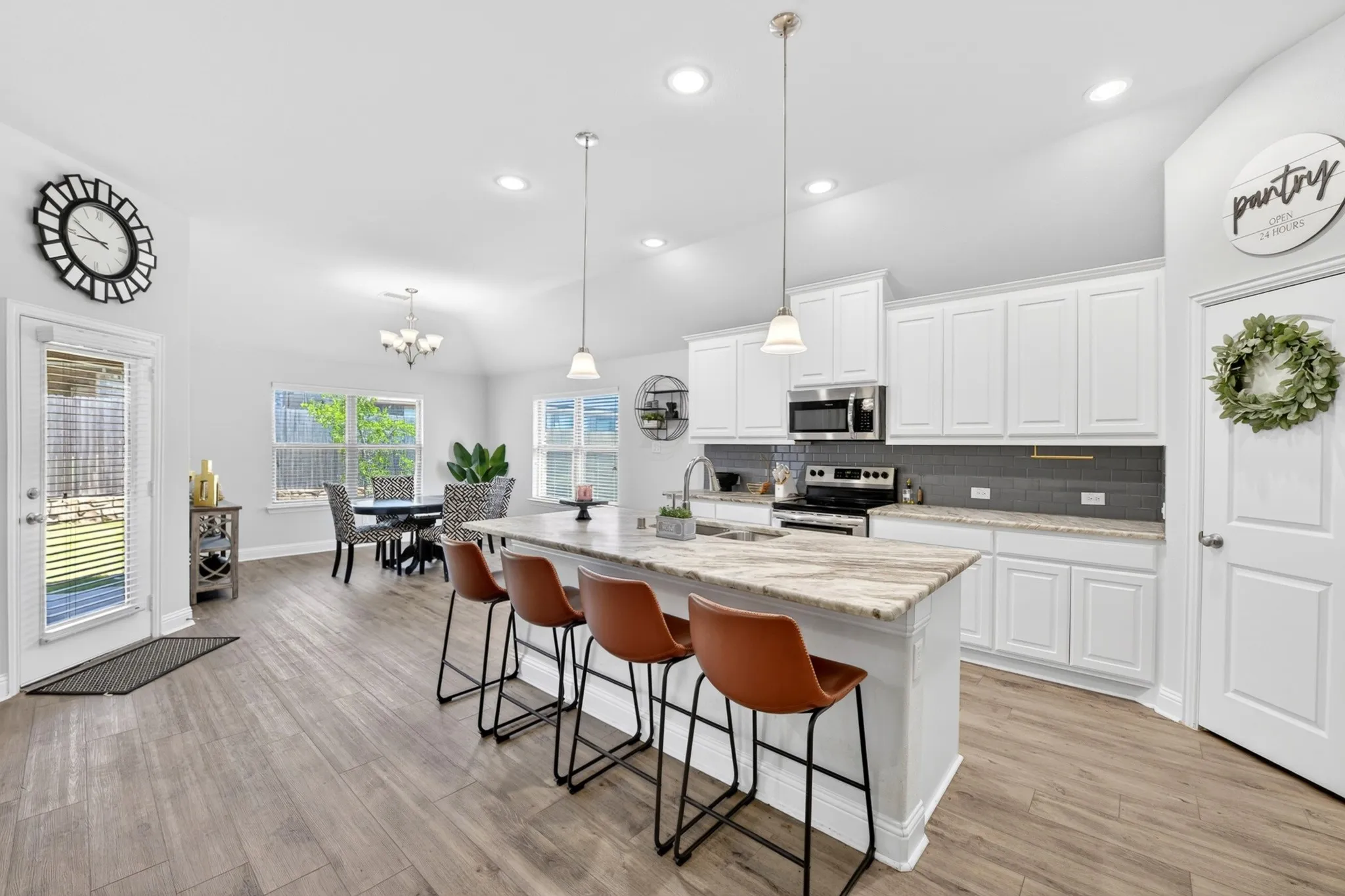 Open-concept kitchen and dining area featuring a central island, white cabinetry, integrated stainless steel appliances, wood-finish flooring, and ample natural light from multiple windows