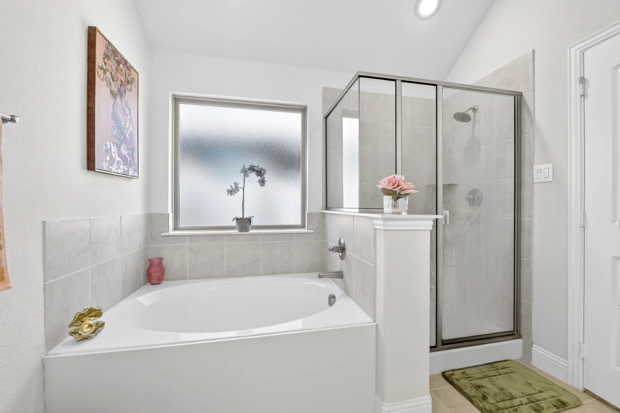 Corner soaking tub with frosted privacy window, adjacent to a glass-enclosed shower with tile surround and integrated shelving