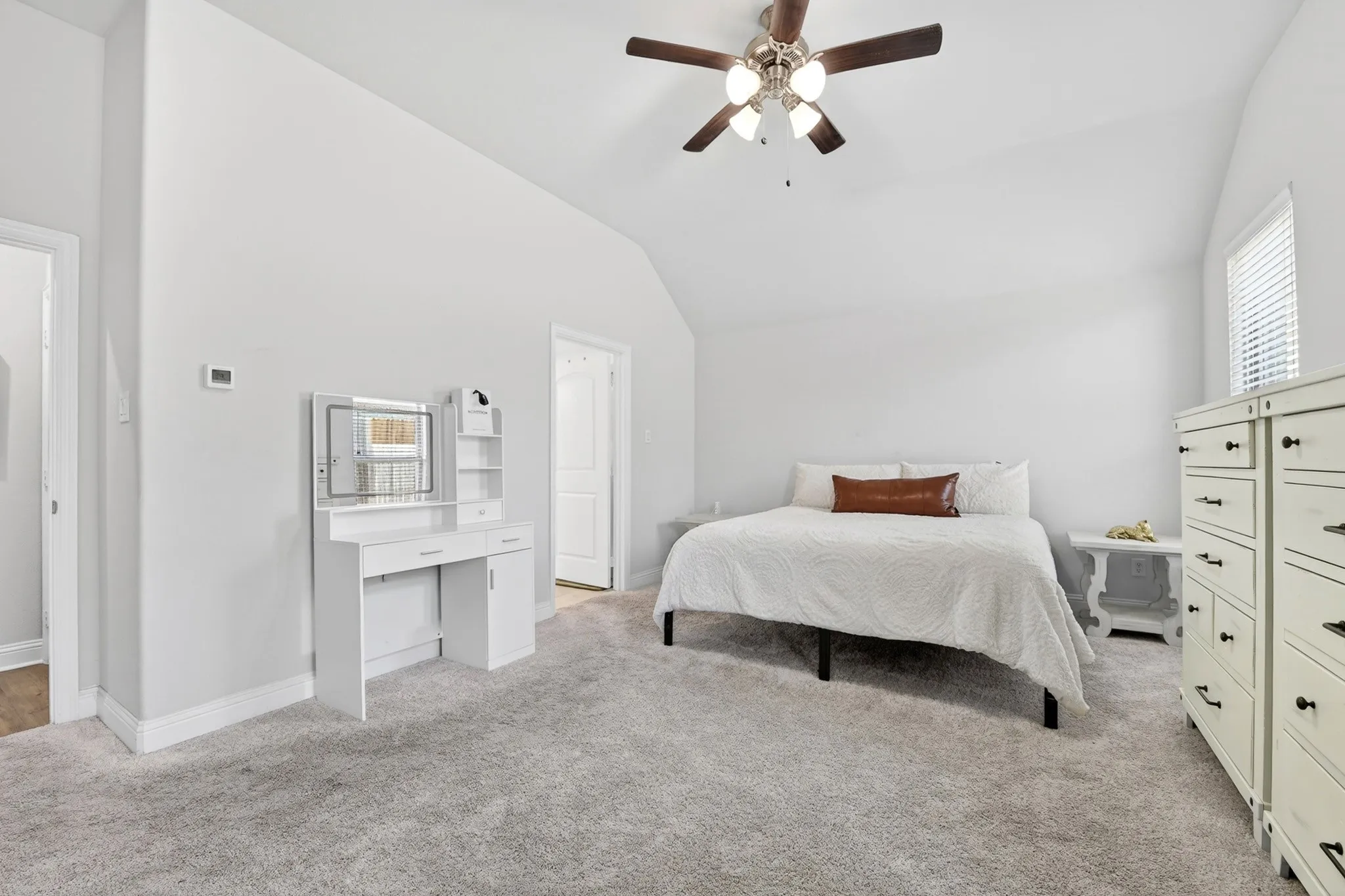 Vaulted ceiling bedroom featuring plush gray carpeting, white walls, a ceiling fan with light kit, and a window with blinds