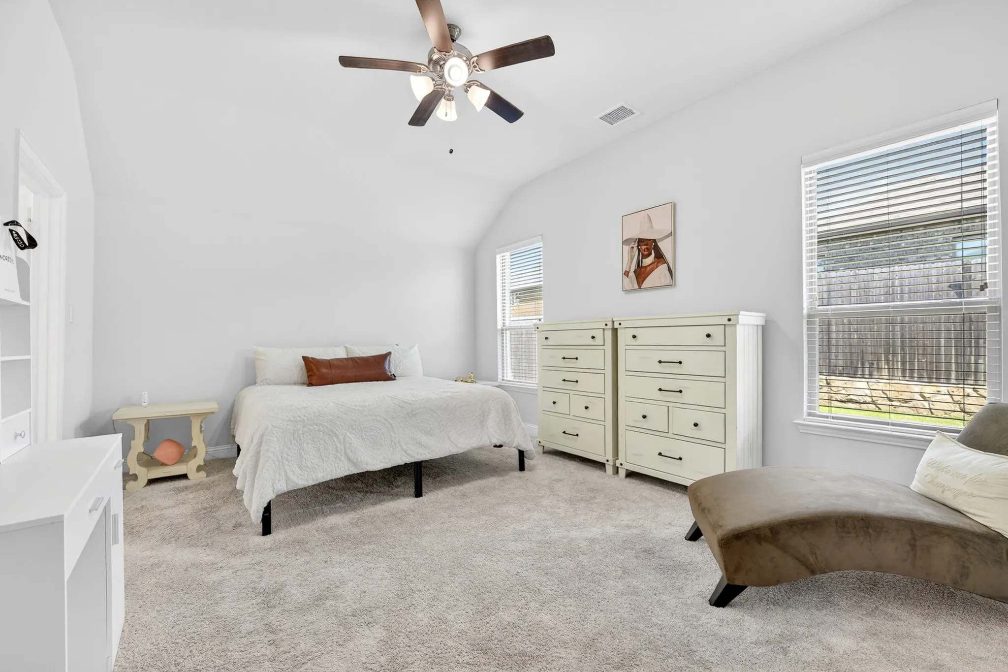Spacious bedroom featuring light neutral wall tones, vaulted ceilings, and plush carpet flooring