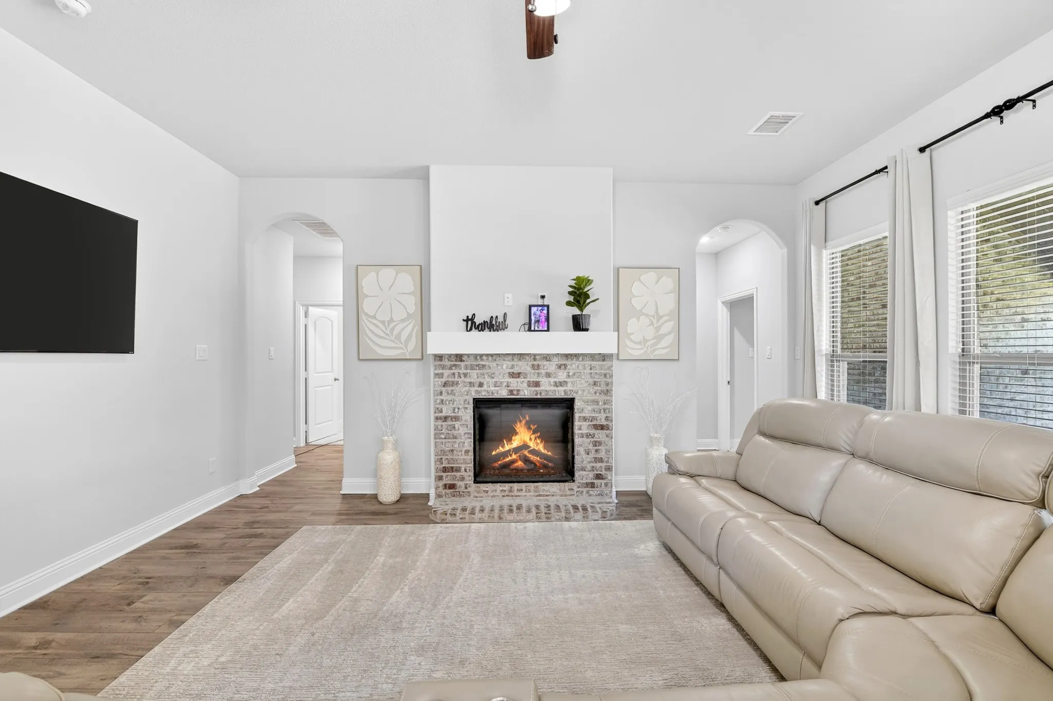 Living area featuring a brick fireplace with a white mantel, wood-finish flooring, and multiple windows
