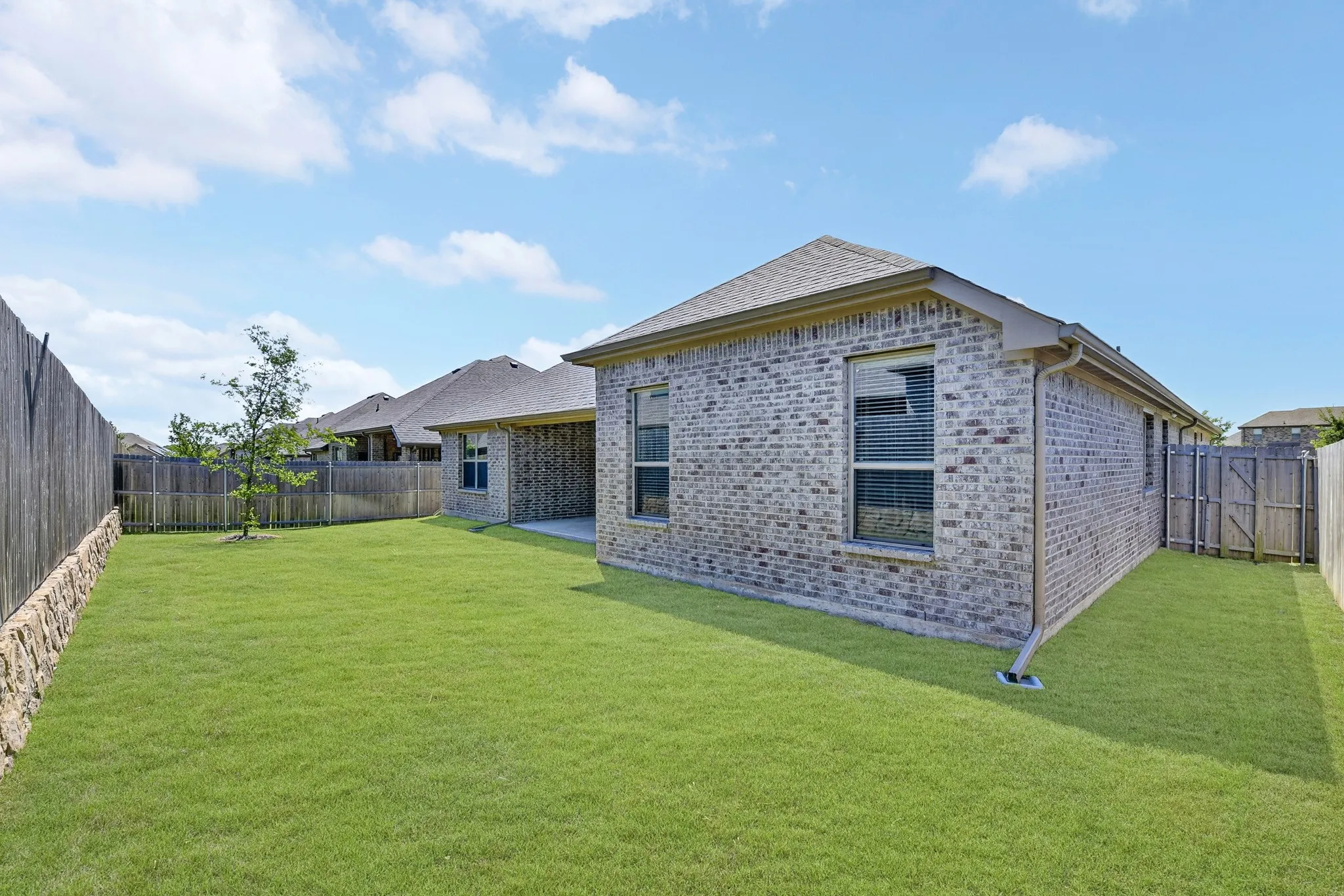 Expansive backyard featuring a manicured lawn, full brick exterior, a covered patio, and privacy fencing
