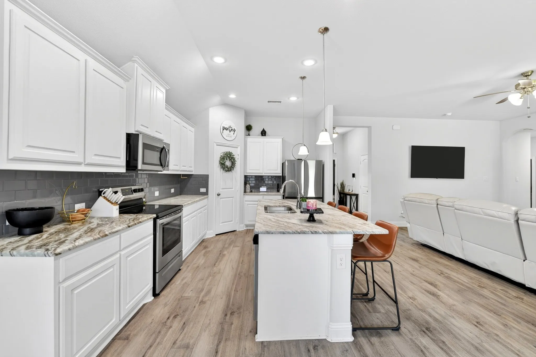 Open-concept kitchen featuring white shaker cabinetry, stainless steel appliances, a dark subway tile backsplash, and wood-finish flooring