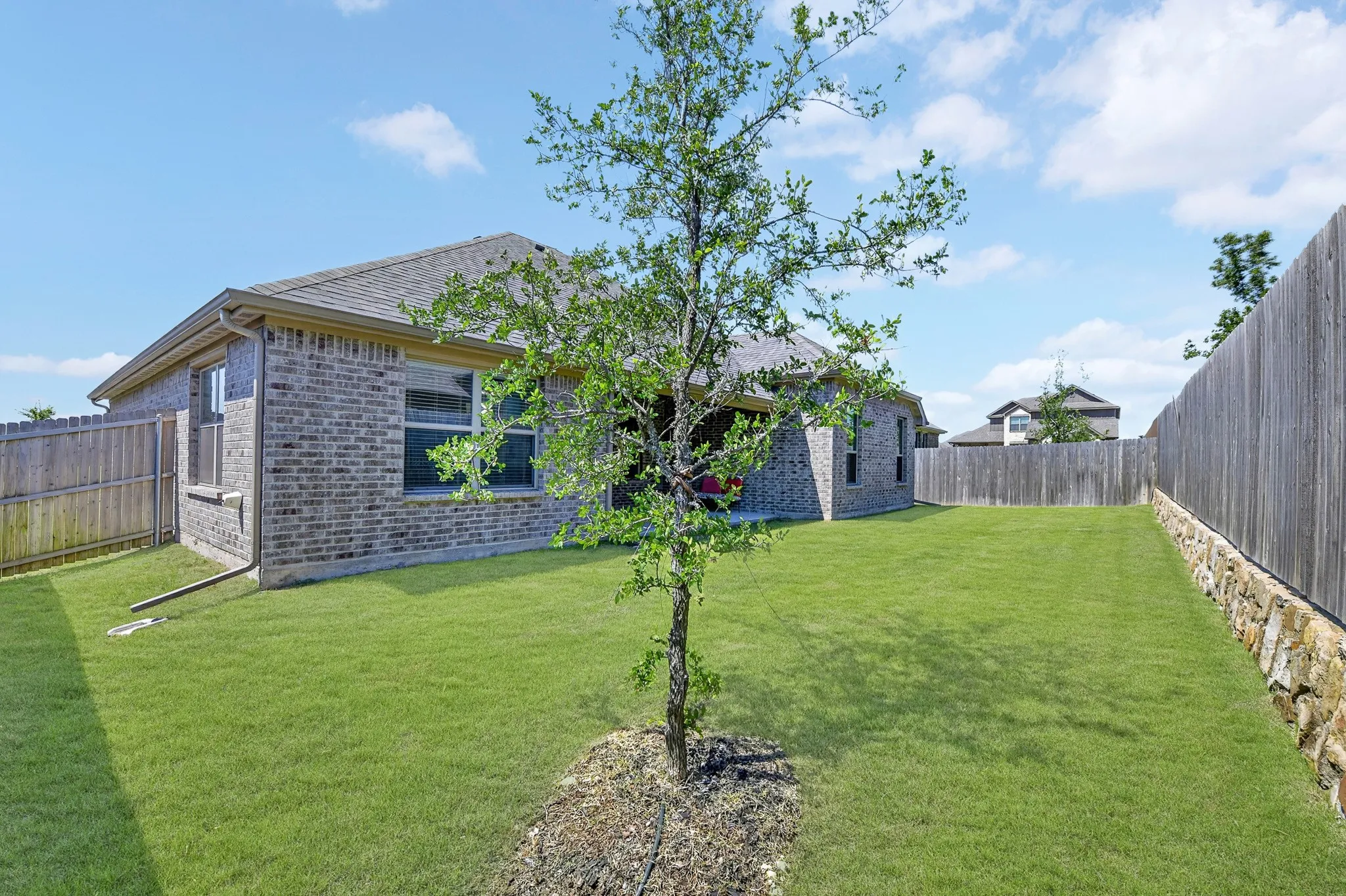 Spacious backyard featuring an extensive lawn, full perimeter fencing, and a retaining wall