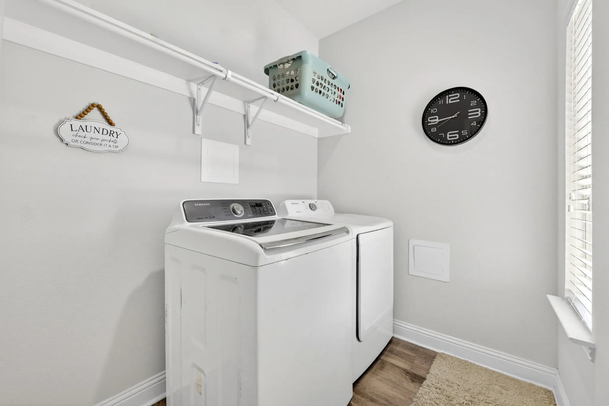 Bright utility space featuring two white appliances, wood-finish flooring, and a window with blinds