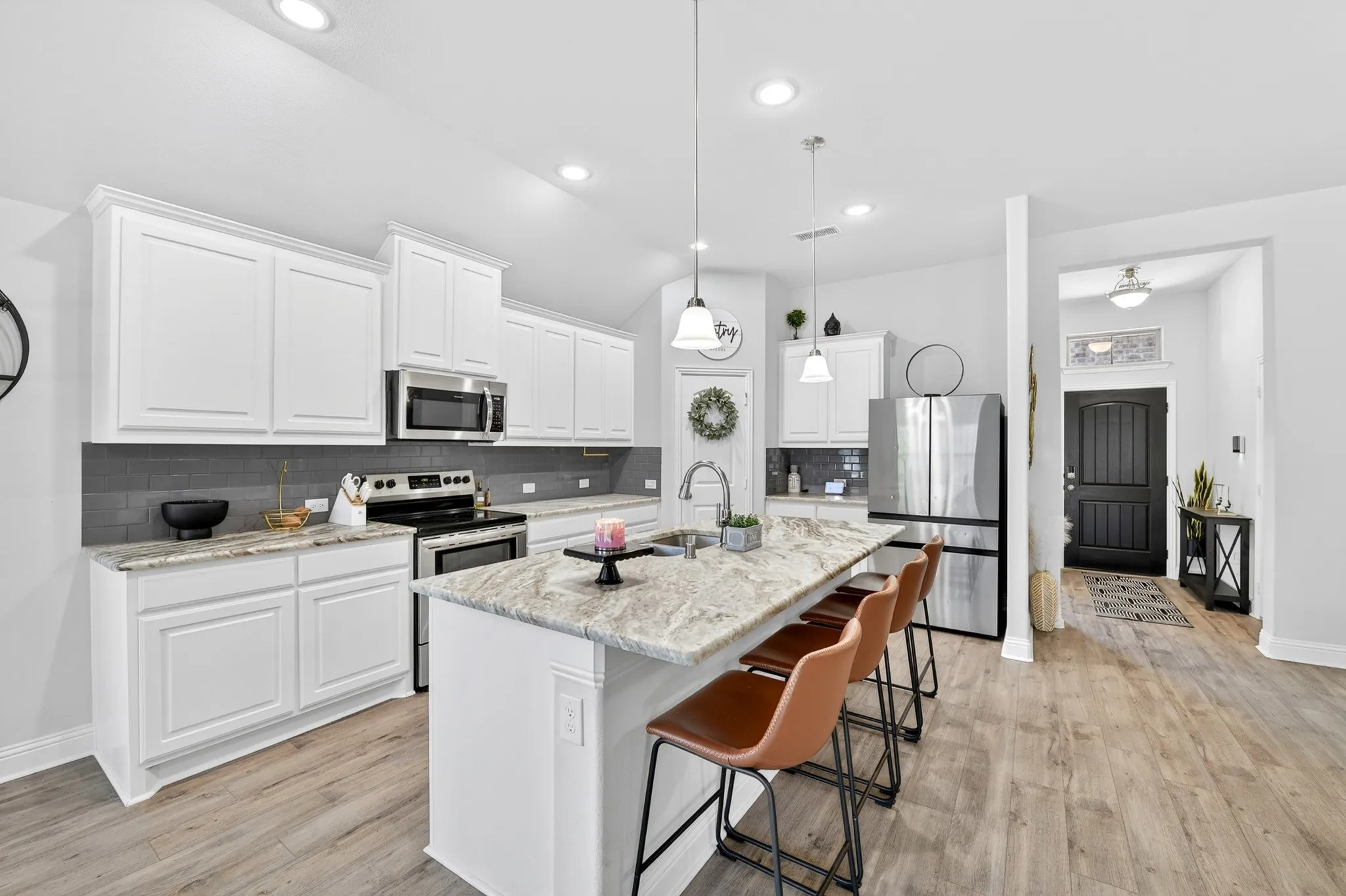 Modern kitchen featuring an expansive island with a light-toned countertop, white cabinetry, stainless steel appliances, and a dark subway tile backsplash
