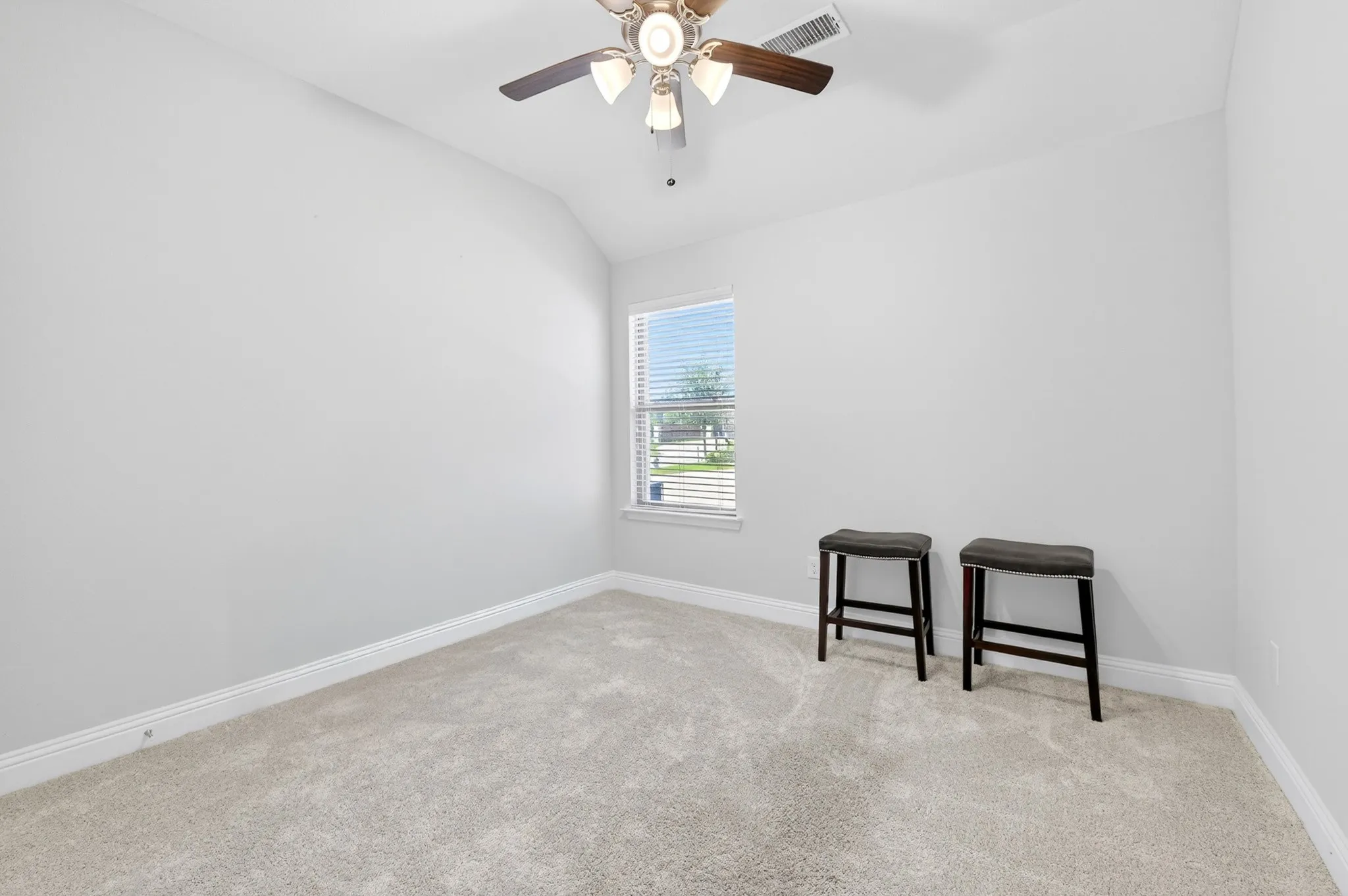Carpeted room featuring a single window with blinds, a ceiling fan with light fixture, white baseboards, and light gray walls