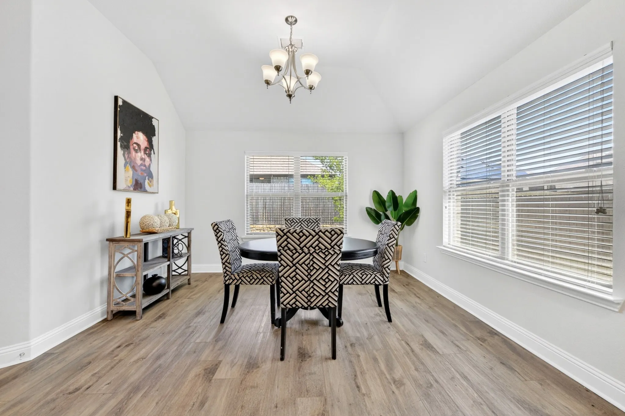 Bright dining area featuring vaulted ceilings, wood-finish flooring, and multiple windows with blinds