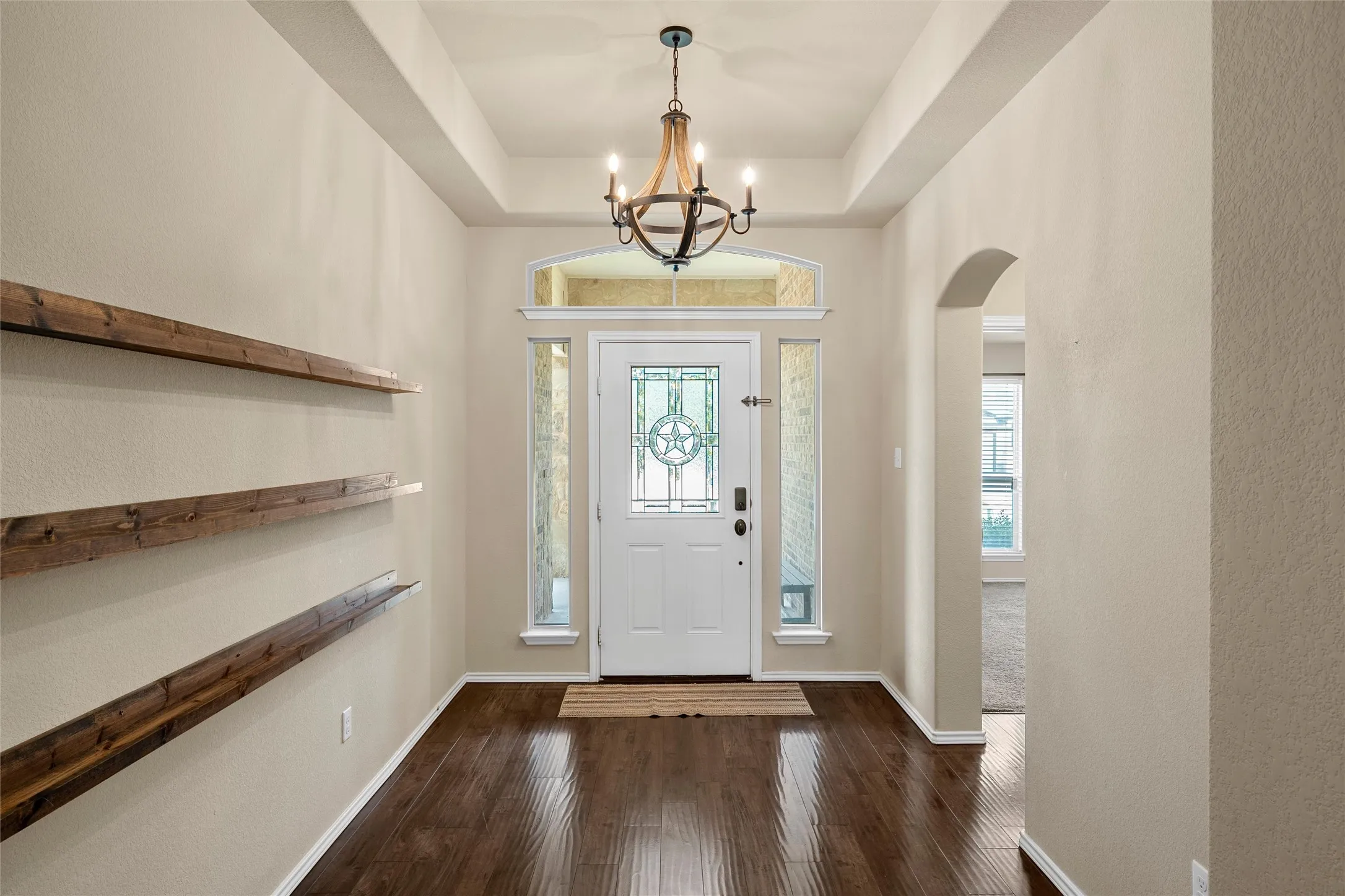 Inviting entry foyer featuring wood-finish flooring, a decorative glass-paneled front door with sidelights and transom, a tray ceiling, and a rustic chandelier