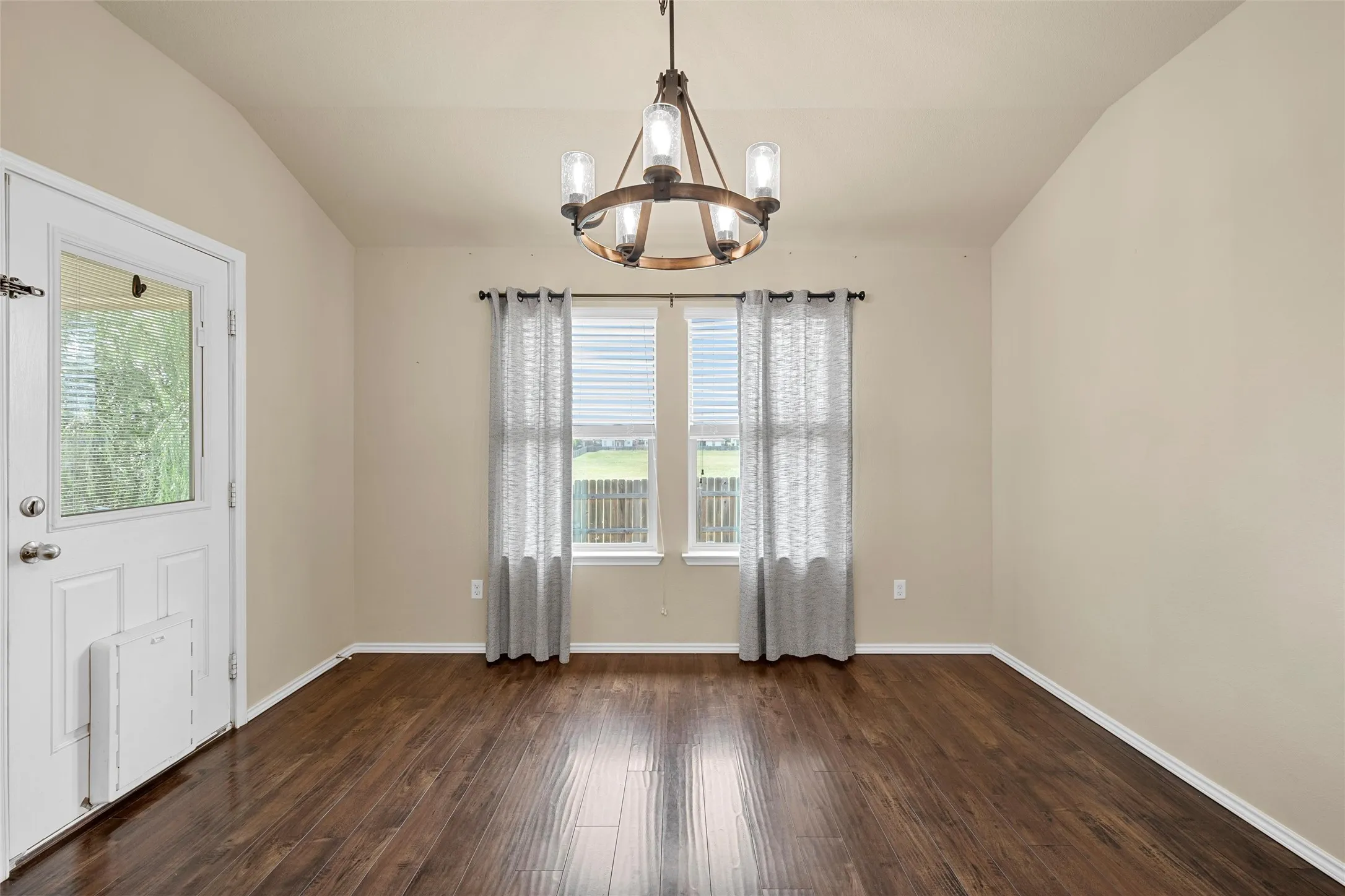 Vaulted ceiling room featuring wood-finish flooring, a rear-facing glass-paneled door, and two rear-facing windows