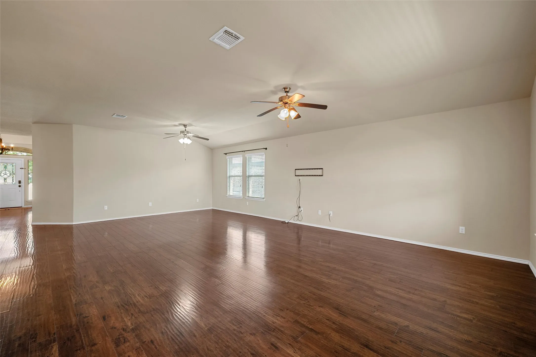 Spacious living area featuring wood-finish flooring, two ceiling fans, and multiple windows providing natural light