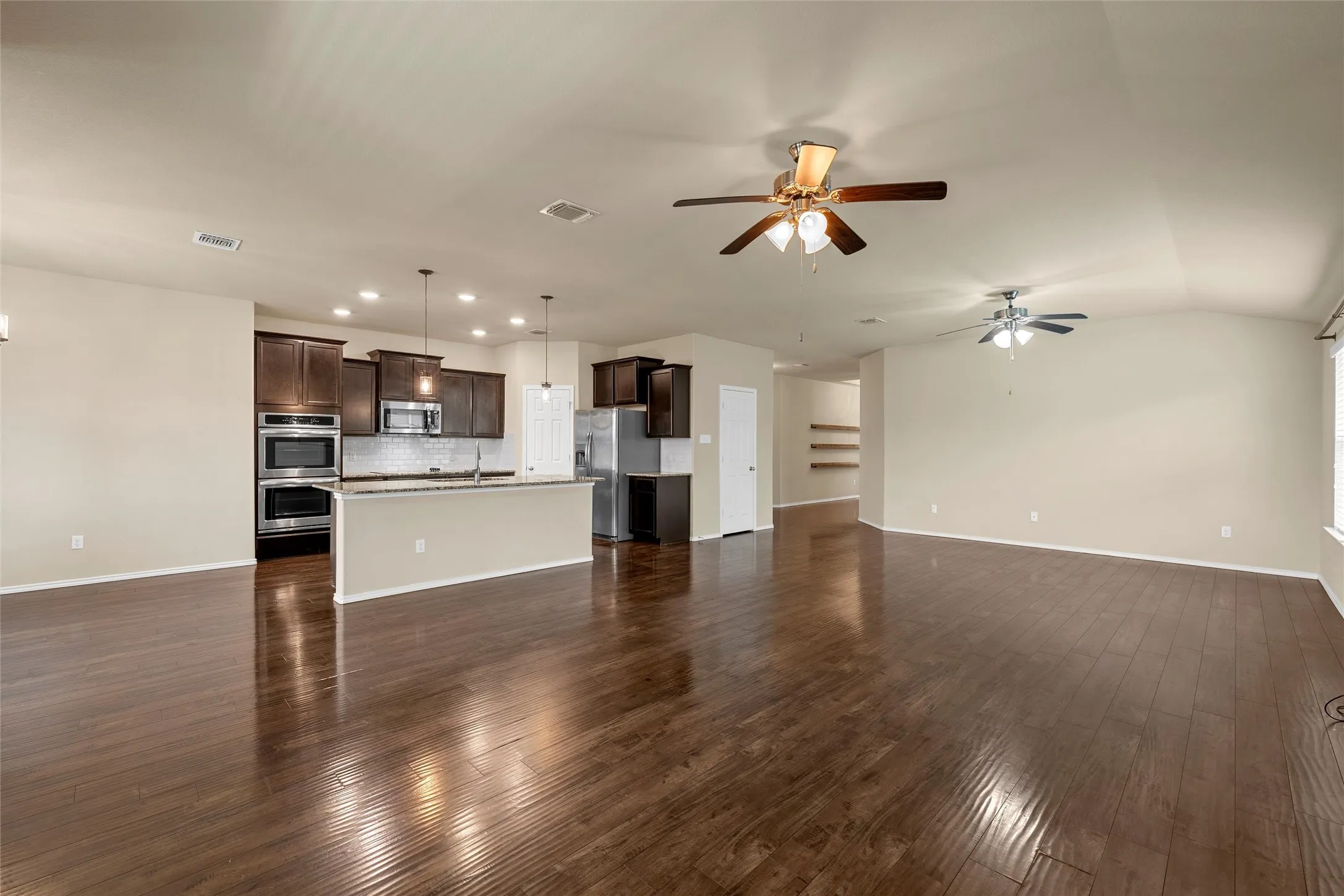 Expansive open concept living area featuring dark wood-finish flooring, two ceiling fans, and neutral wall tones