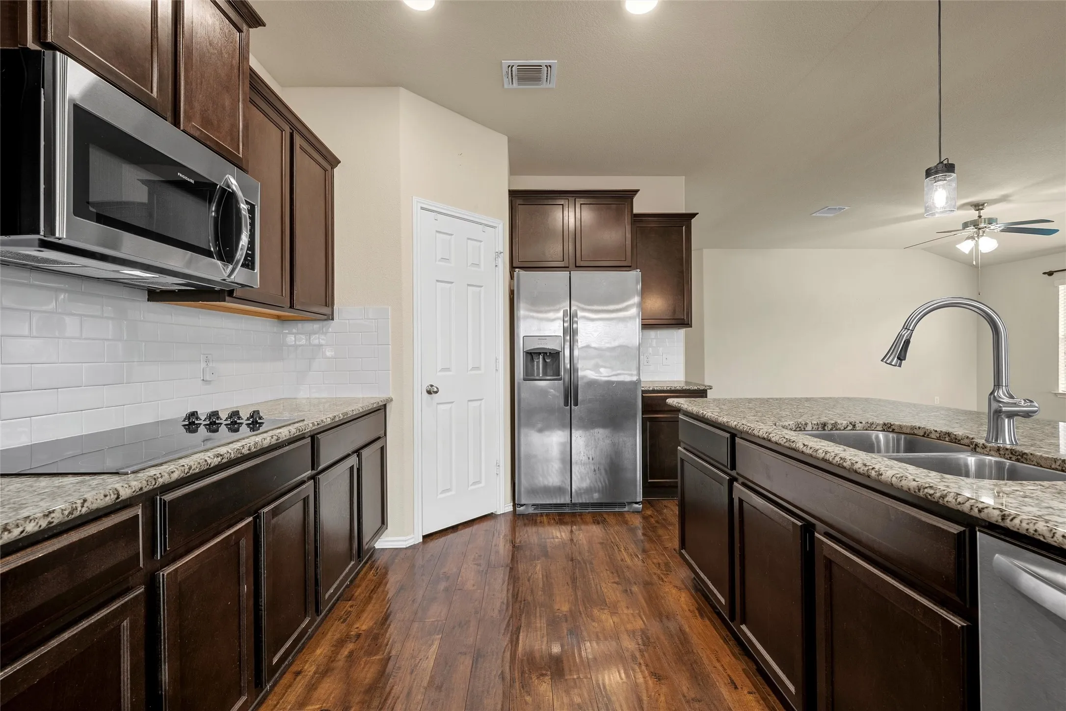 Kitchen featuring rich wood-finish flooring, dark wood cabinetry, granite countertops, and stainless steel appliances