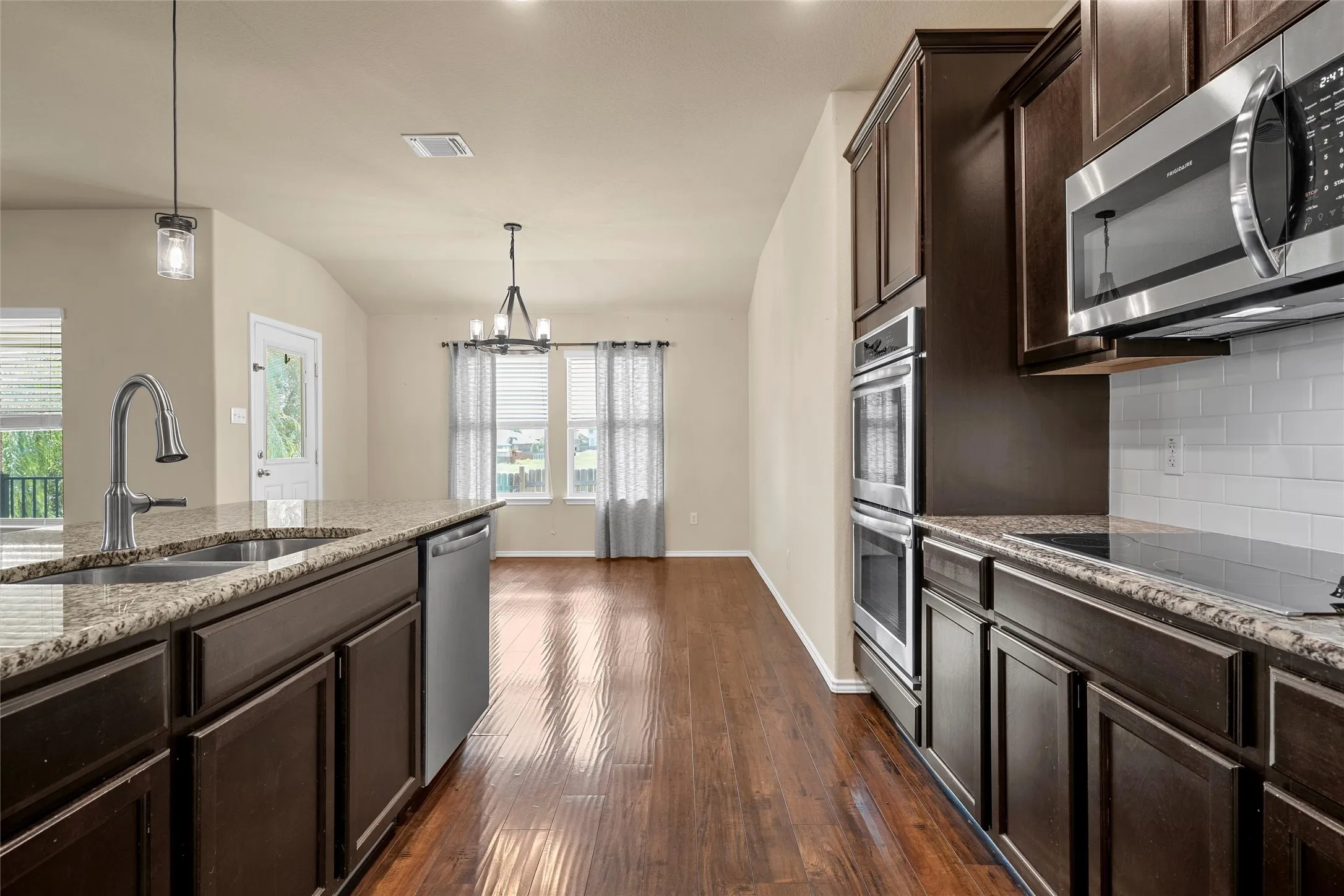 Spacious kitchen featuring rich wood-finish cabinetry, granite countertops, and stainless steel appliances including a built-in double oven and microwave