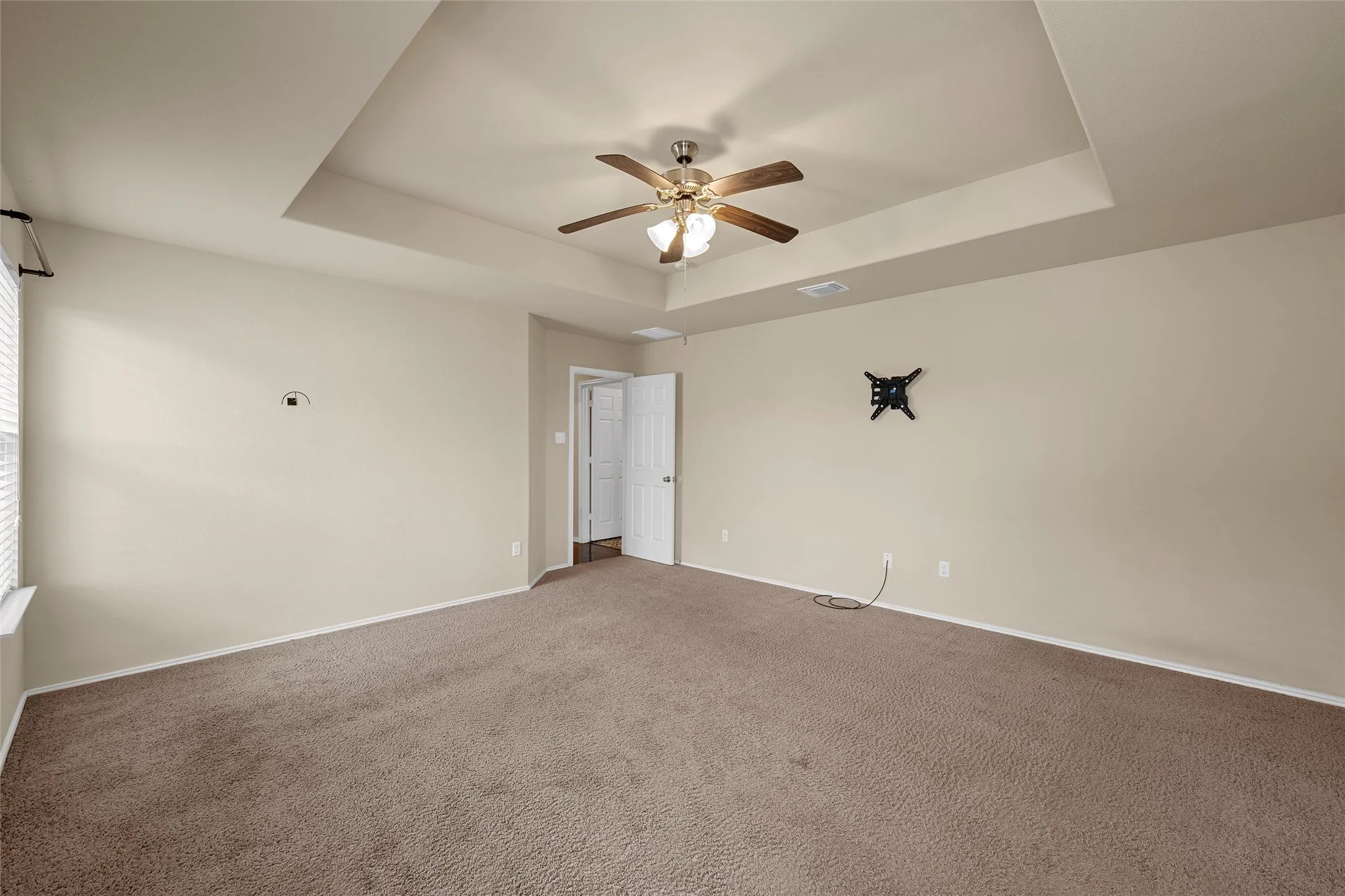 Spacious room featuring a tray ceiling with a ceiling fan, neutral wall paint, and carpet flooring