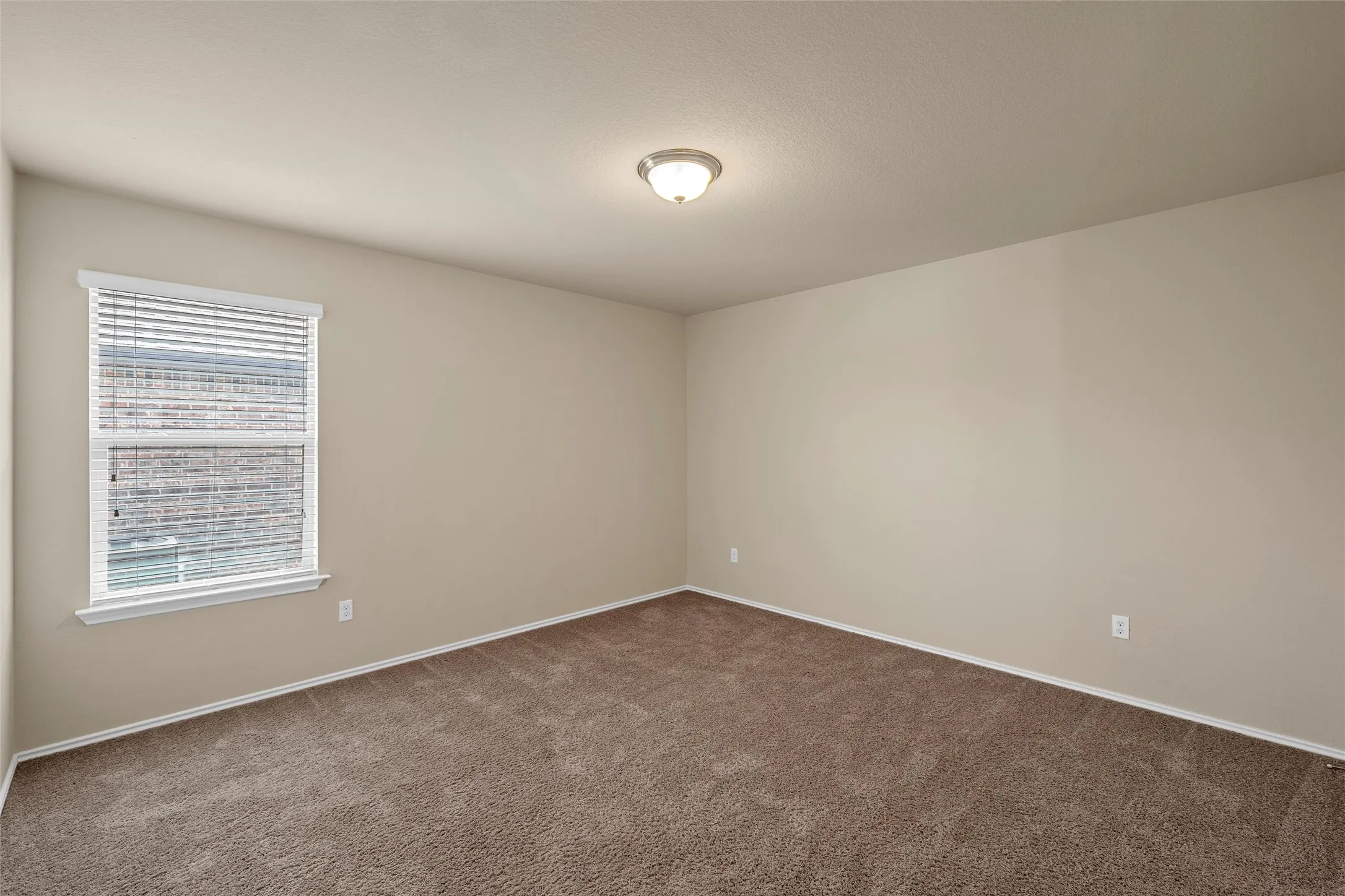 Room featuring neutral wall paint, brown carpet, a single window with white blinds, and a flush-mount ceiling light fixture