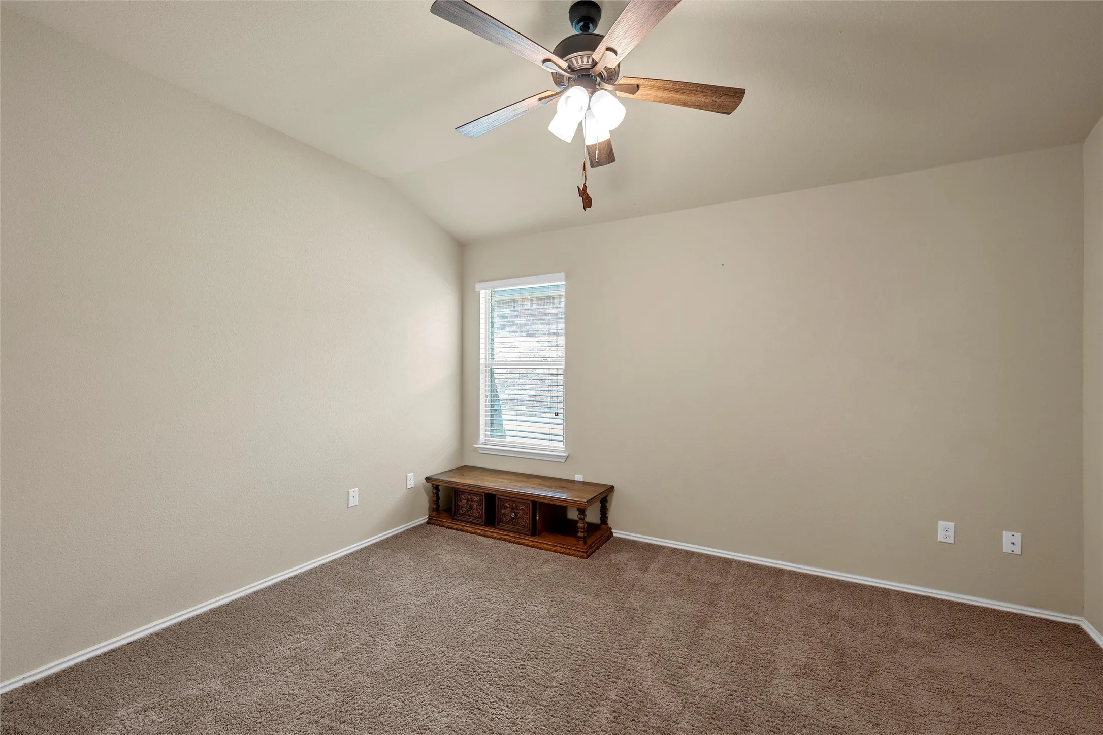 Vaulted ceiling room featuring neutral-toned walls, brown carpet, and a window with blinds