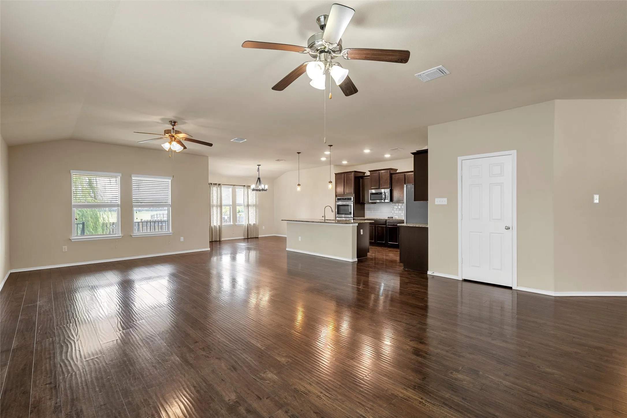 Expansive interior featuring rich wood-finish flooring, vaulted ceilings, and multiple windows with blinds