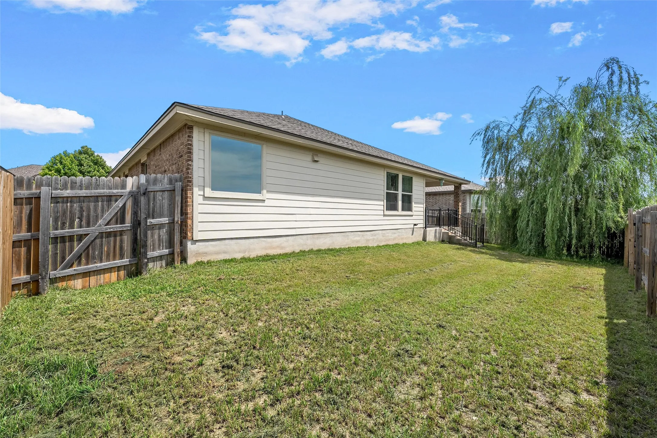 Expansive rear yard featuring a manicured lawn, full privacy fencing, and a mature weeping willow tree