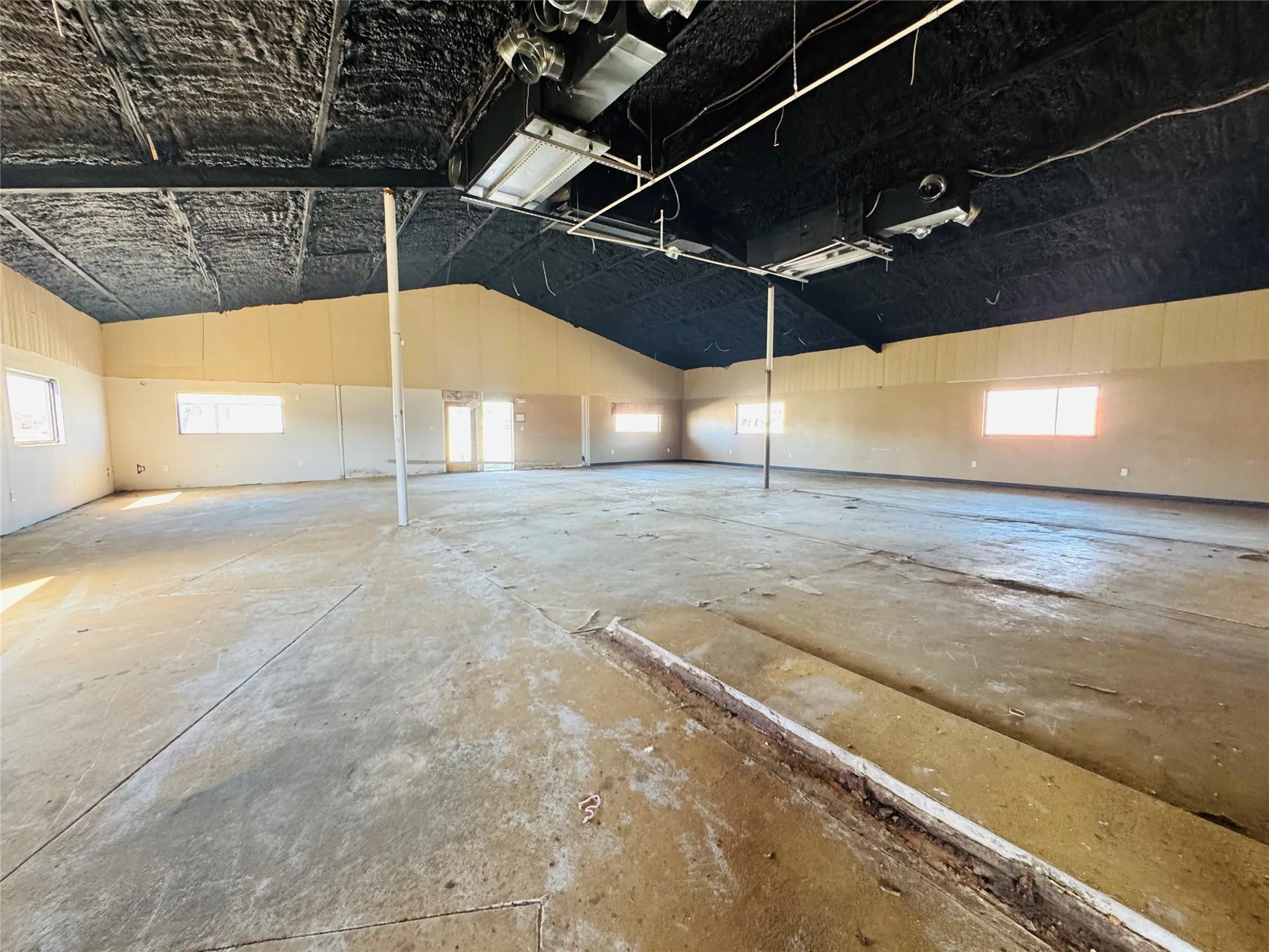 Expansive interior space featuring a concrete floor, high vaulted ceiling with exposed ductwork, and multiple windows providing ambient light
