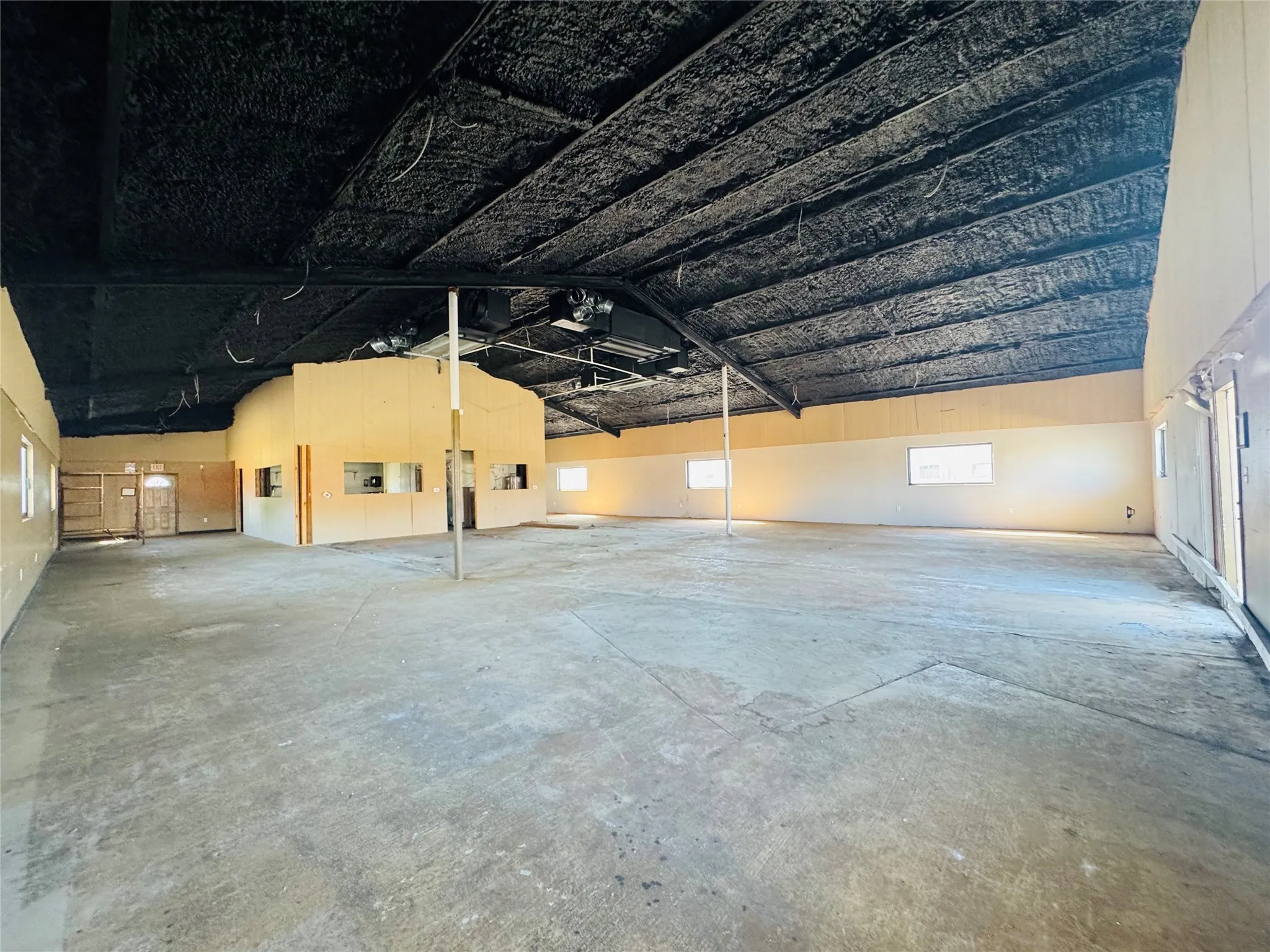 Expansive interior space featuring concrete flooring, a high, textured ceiling with exposed structural elements, and multiple windows