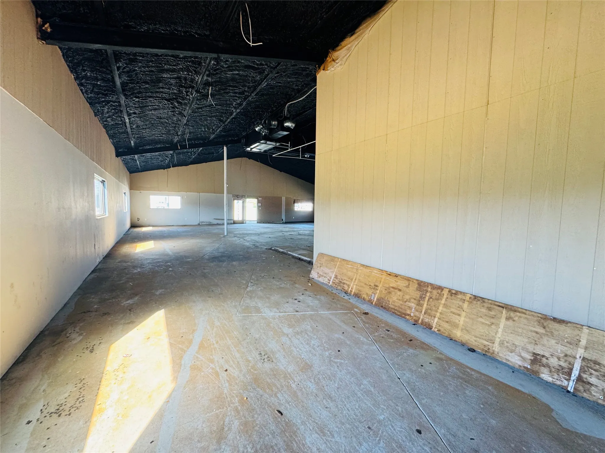 Spacious interior featuring a high vaulted ceiling with exposed structure, concrete flooring, and multiple windows allowing natural light