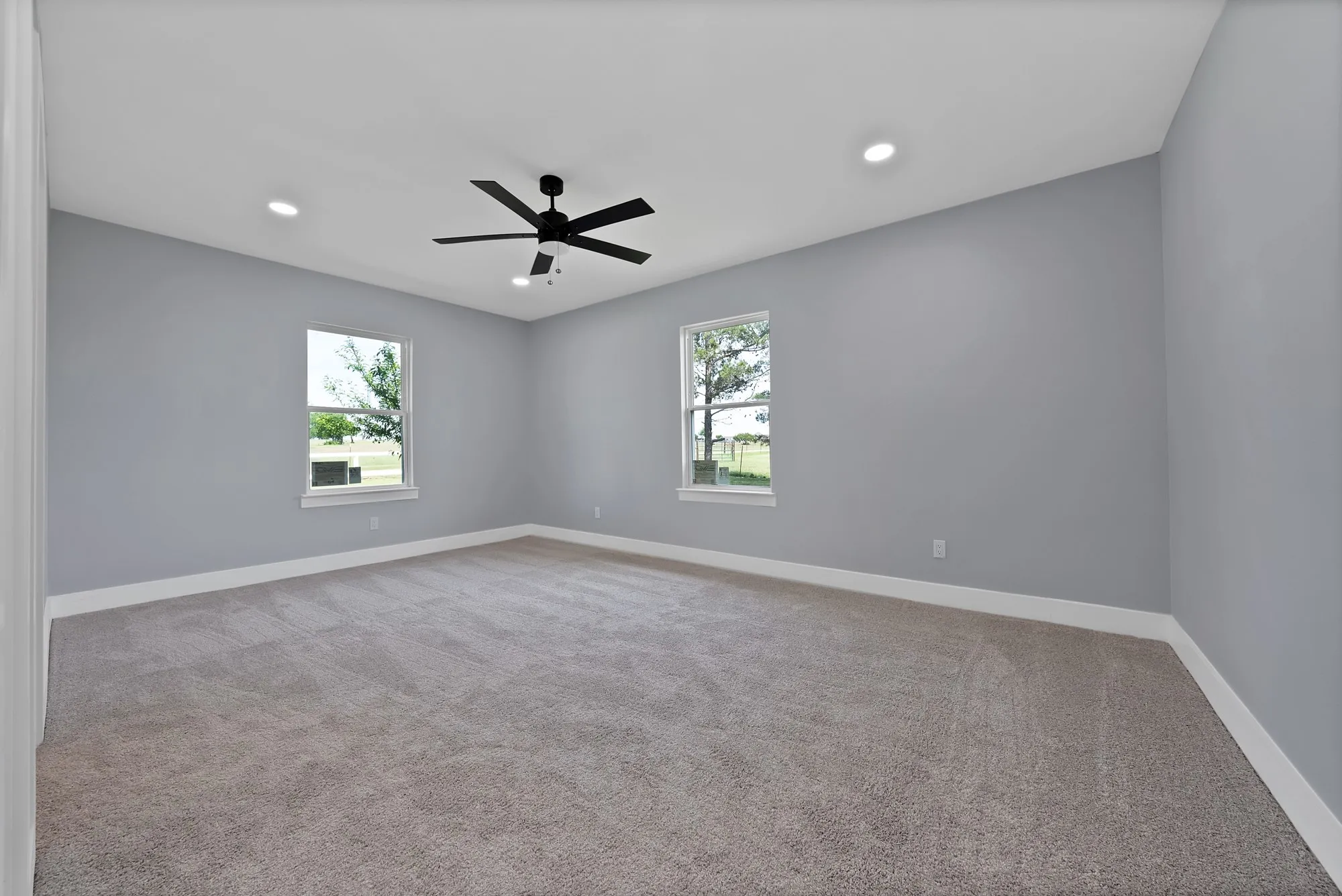 Spacious room featuring light gray walls, plush carpeting, two windows, recessed lighting, and a ceiling fan with integrated lighting