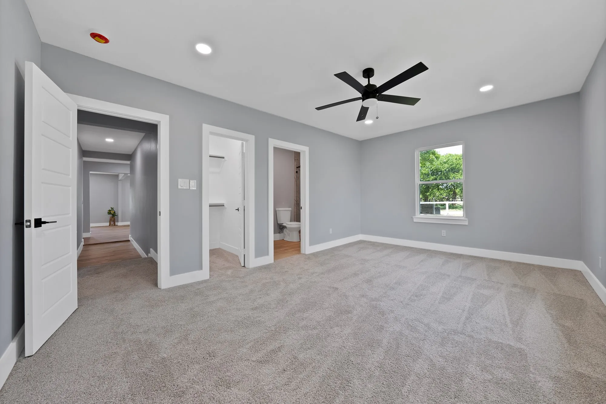 Spacious carpeted room featuring a ceiling fan with integrated lighting, recessed lighting, and a window with exterior tree views