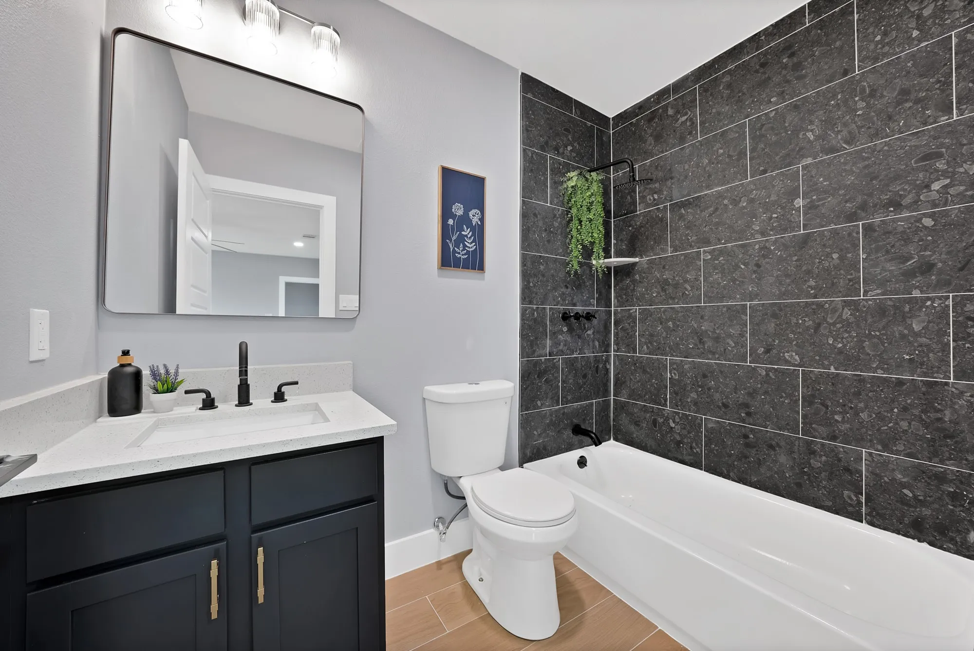 Contemporary bathroom featuring a dark tile bath surround, white porcelain bathtub, and a dark vanity with a white countertop