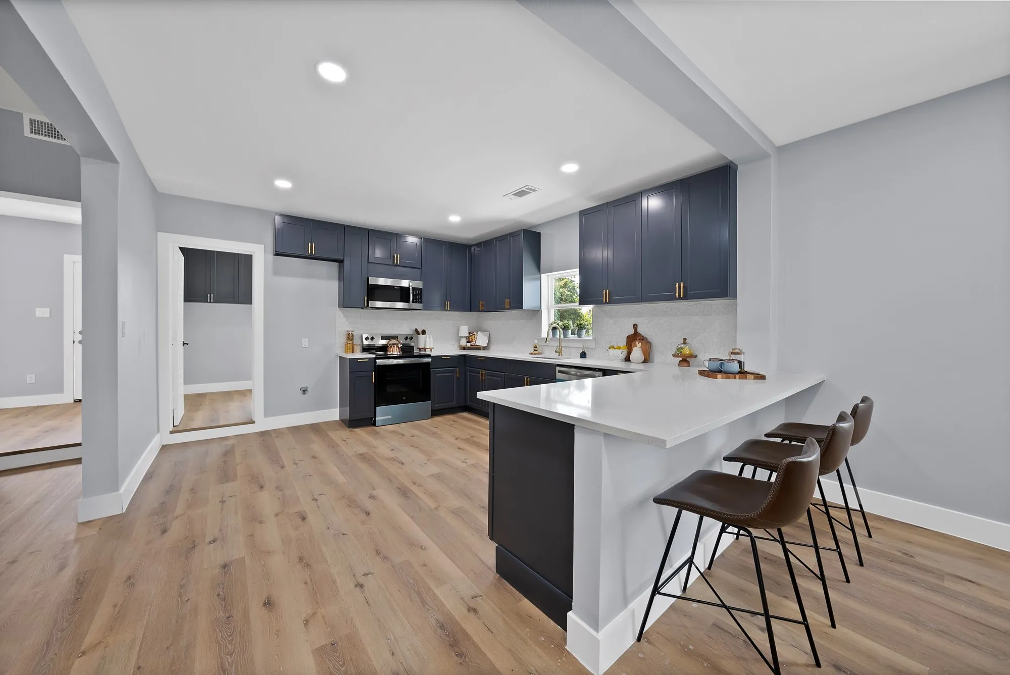 Kitchen featuring blue-grey cabinetry, light wood-finish flooring, recessed lighting, and a white countertop island with seating