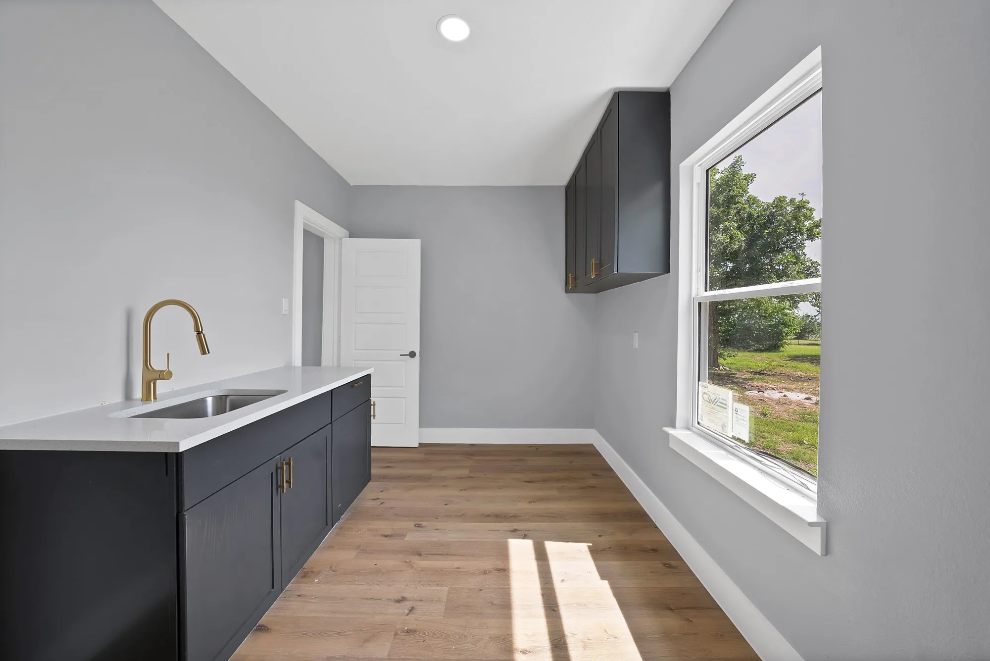 Utility room featuring a built-in sink with a gooseneck faucet, dark cabinetry, and light wood-finish flooring