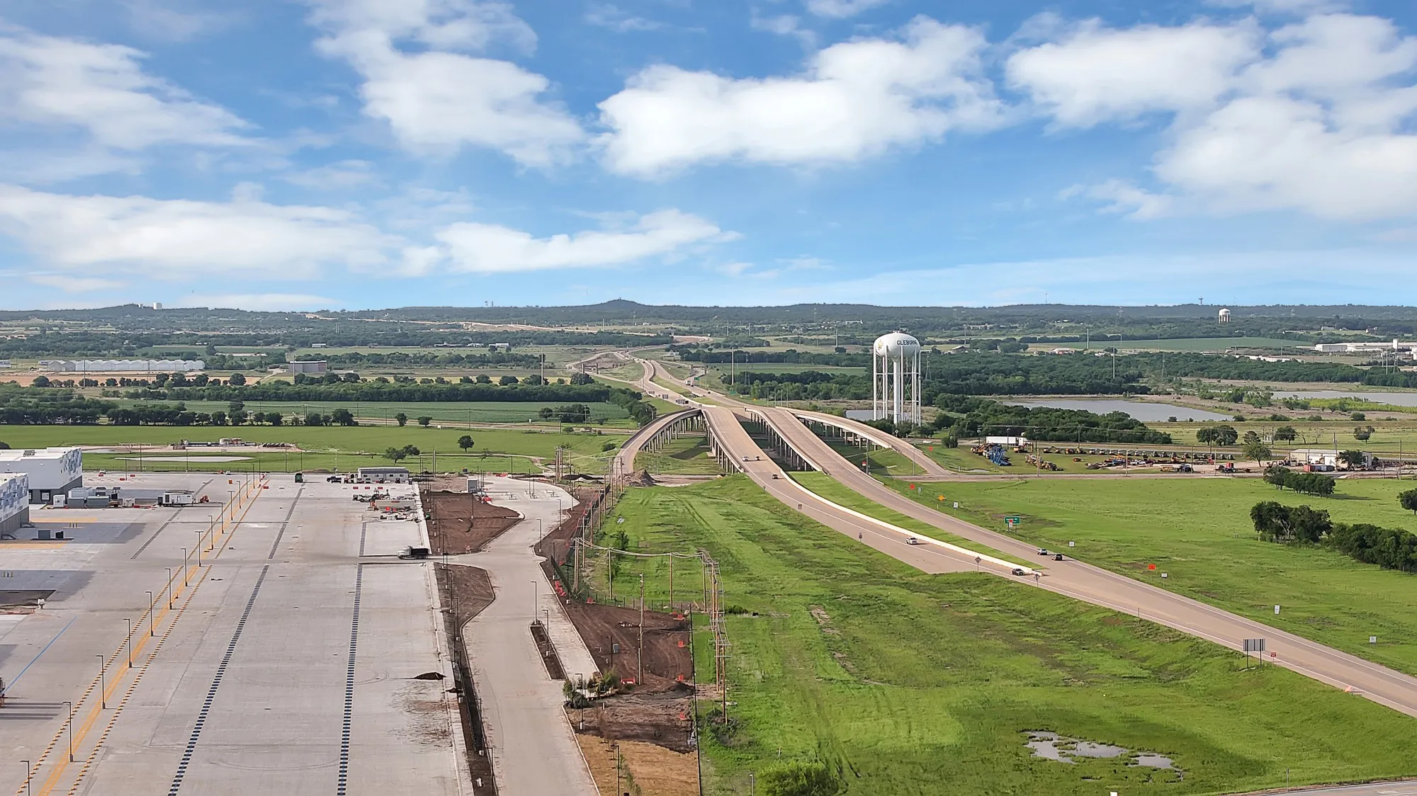 Expansive paved lot with visible highway infrastructure, surrounding green areas, and a distant water tower