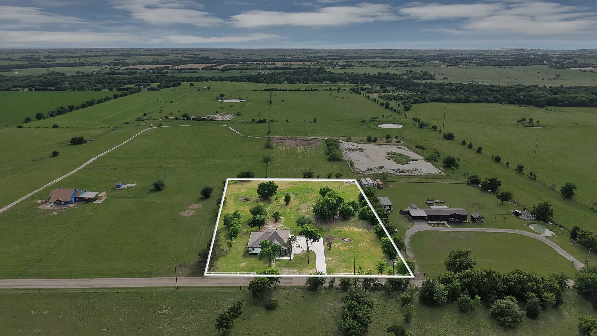 Expansive lot featuring a single-story home with a light-colored roof, surrounded by mature trees and verdant lawns
