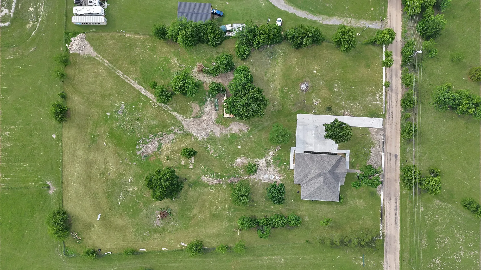 Aerial perspective of a single-story residence with a gray shingle roof, situated on a substantial grassy parcel